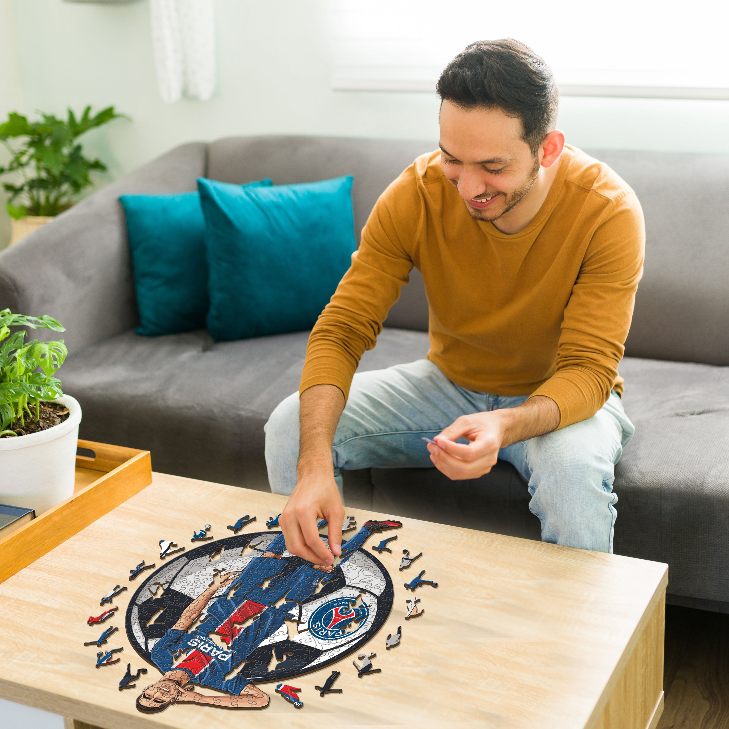 Mann im senfgelben Pullover baut Puzzle mit Fußballspieler auf Holztisch.