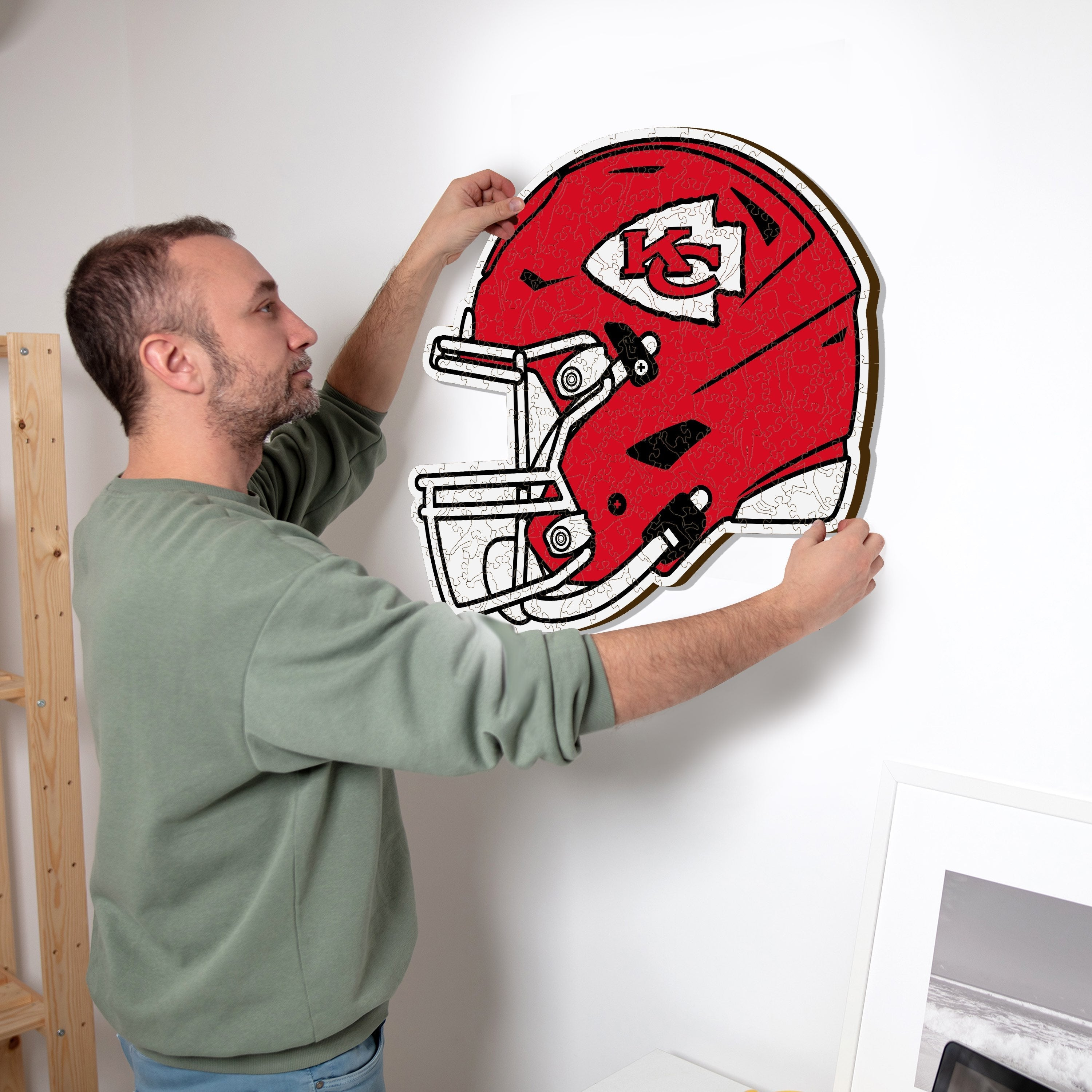 Ein Mann hängt ein rotes Footballhelm-Puzzle mit einem K-Logo an die Wand.