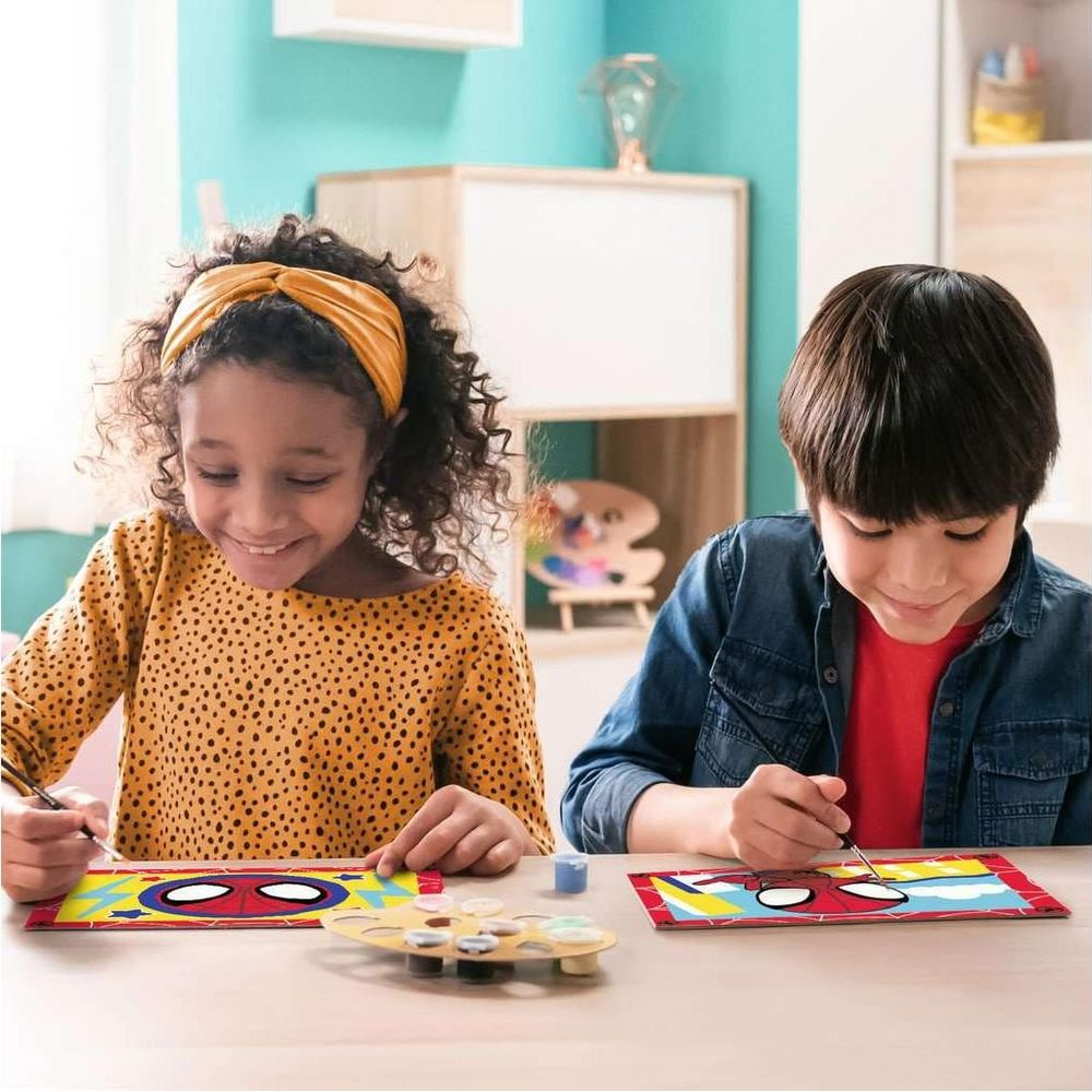 Dos niños pintan cuadros de Spider-Man con pinturas y pinceles en una mesa.