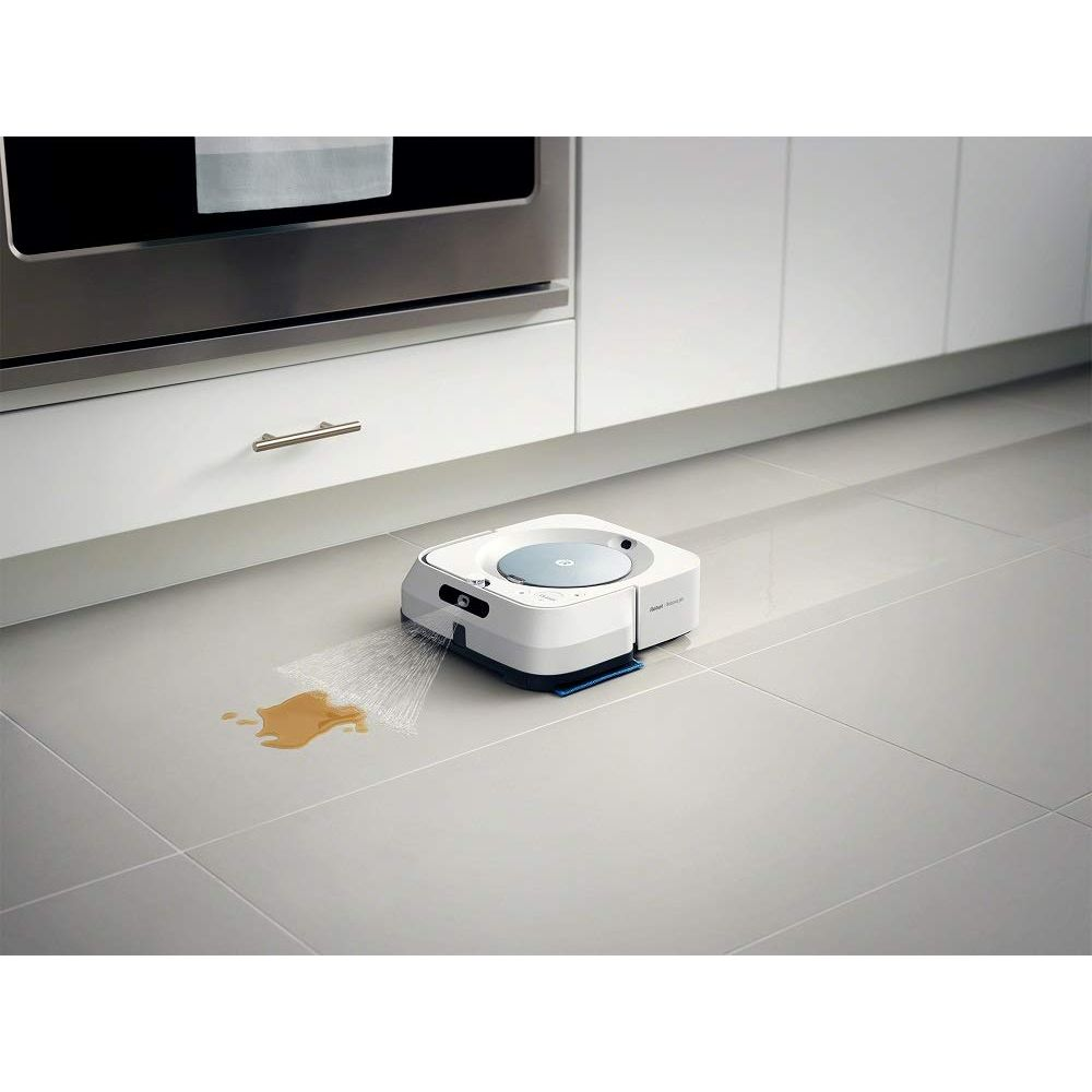Un robot aspirador blanco limpia una mancha marrón derramada en un suelo gris.