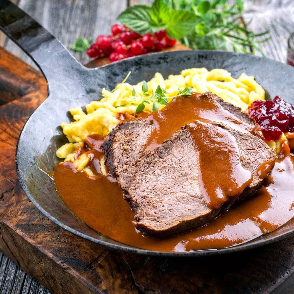 Geschnittenes Bratenfleisch in brauner Soße mit Spätzle und Preiselbeeren.