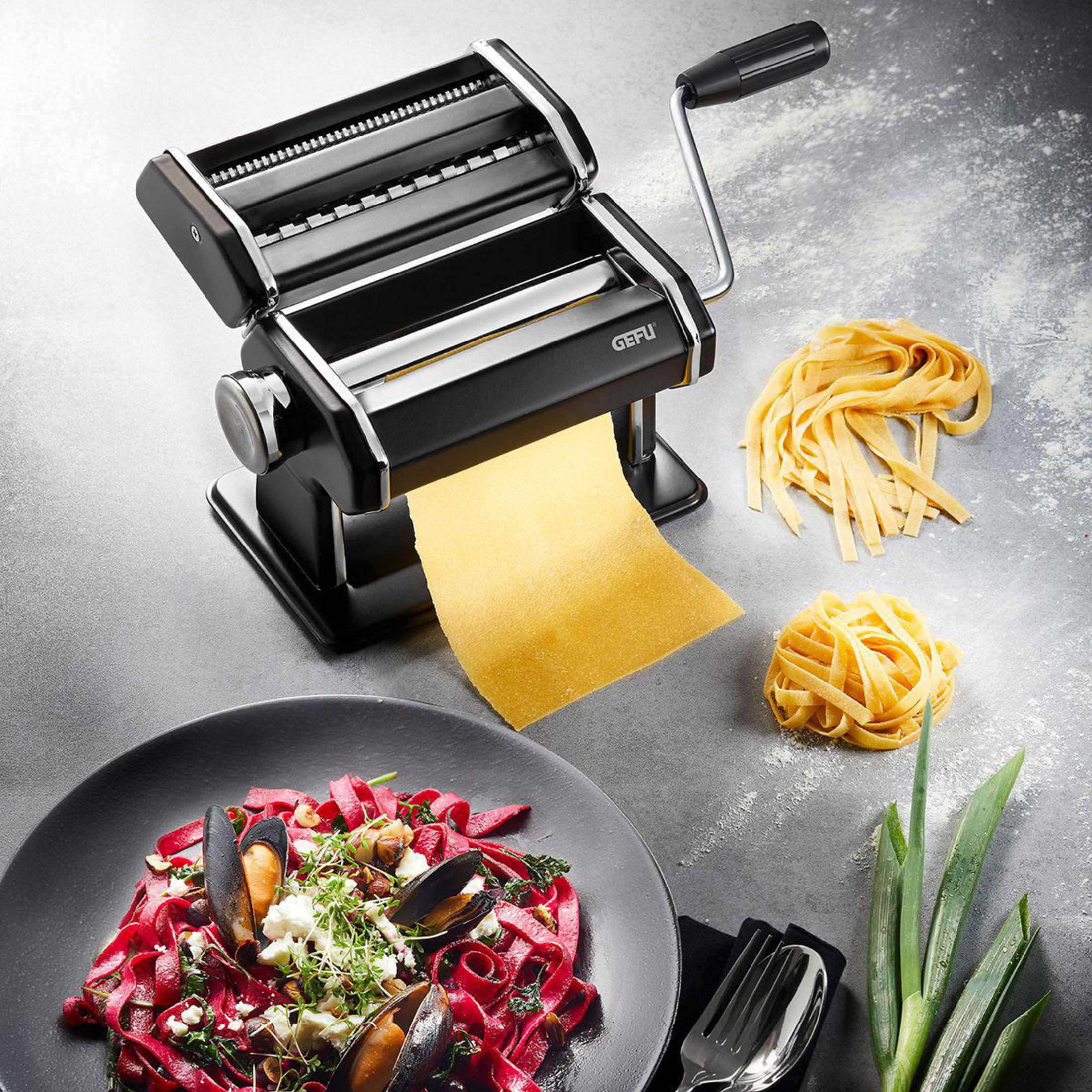 Une machine à pâtes noire avec une feuille de pâte, des pâtes et une assiette de pâtes.