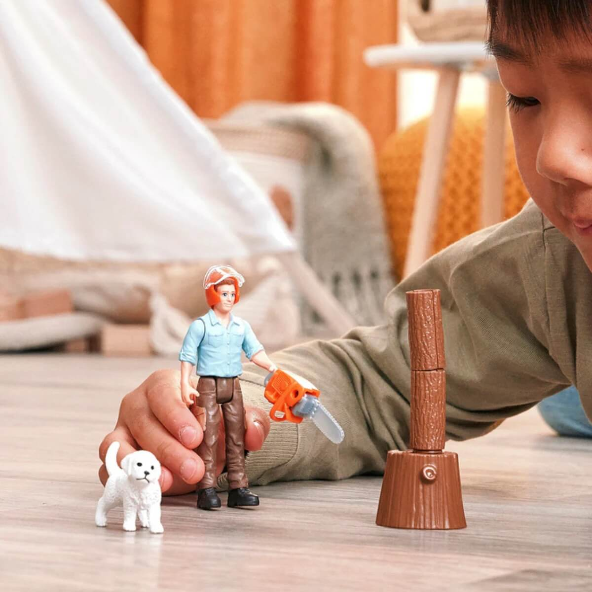 Ein Junge spielt mit Spielzeugfiguren: ein Mann mit Kettensäge, ein Hund und ein Holzstamm.
