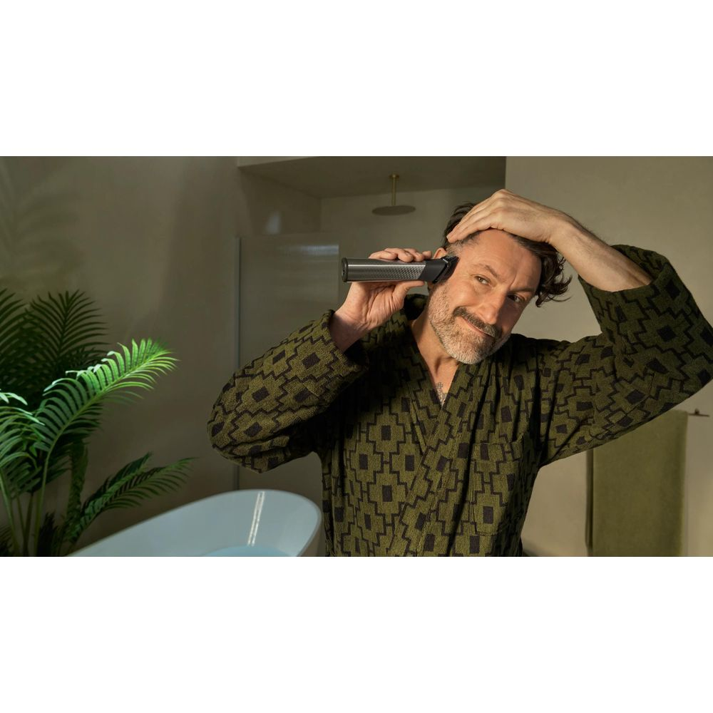 Ein Mann in einem grünen Bademantel trimmt sein Haar mit einem Trimmer.