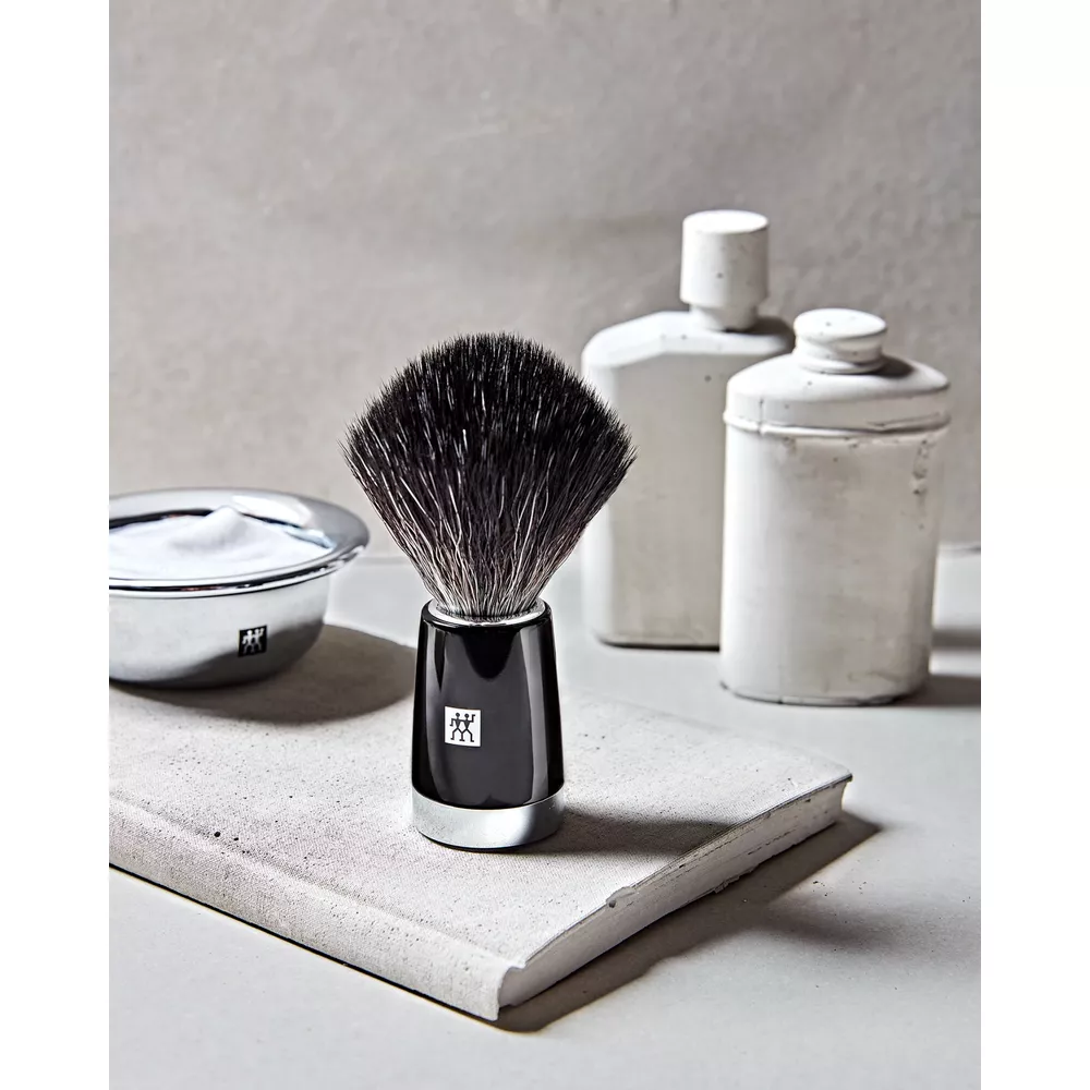 Pennello da barba nero con accenti argentati accanto a una ciotola di schiuma da barba.