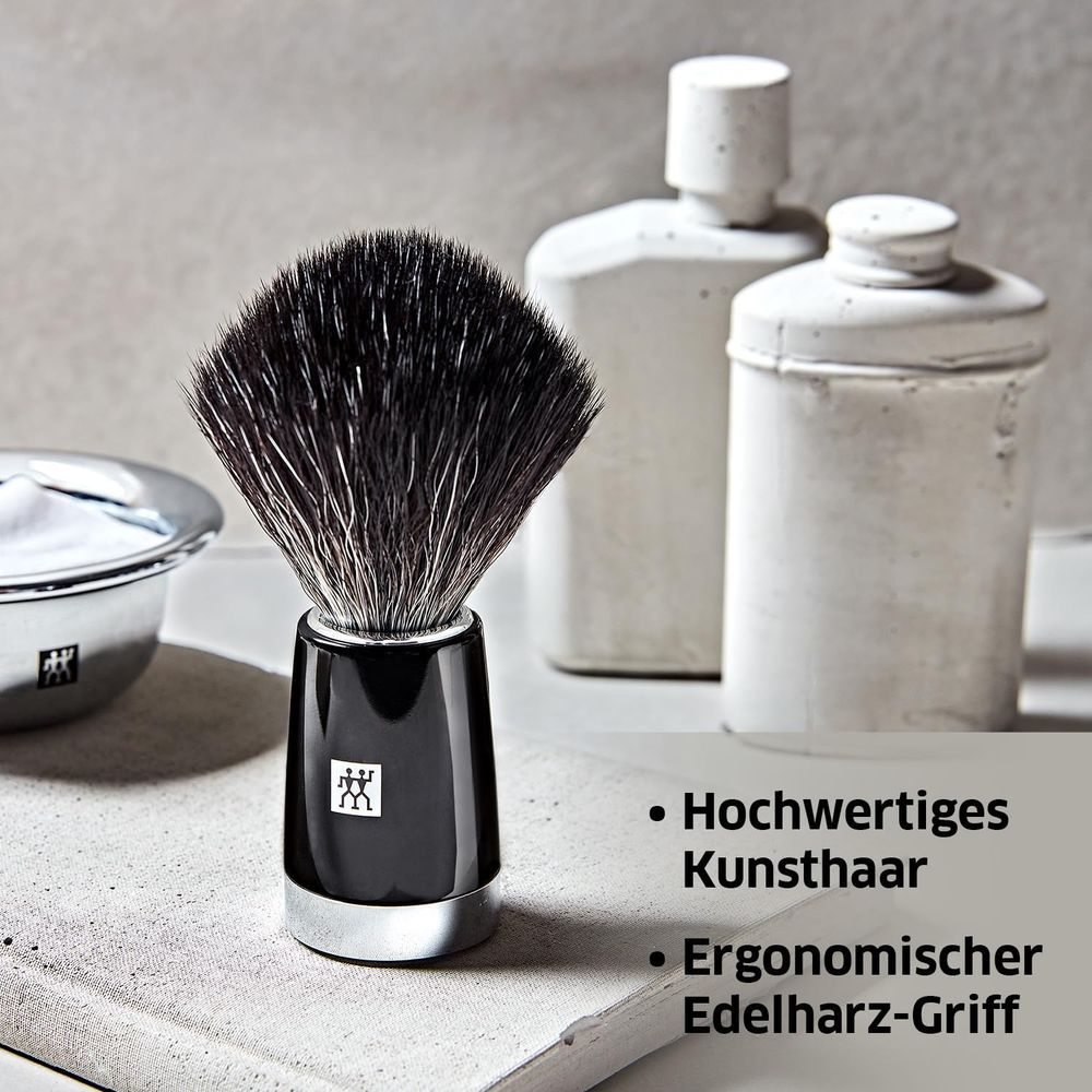 Pennello da barba nero con bordo argentato e contenitori bianchi sullo sfondo.