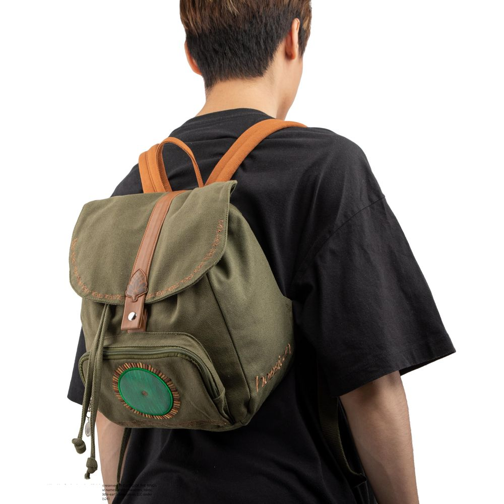 Eine Person trägt einen grünen Canvas-Rucksack mit braunen Lederakzenten und einem runden grünen Emblem.