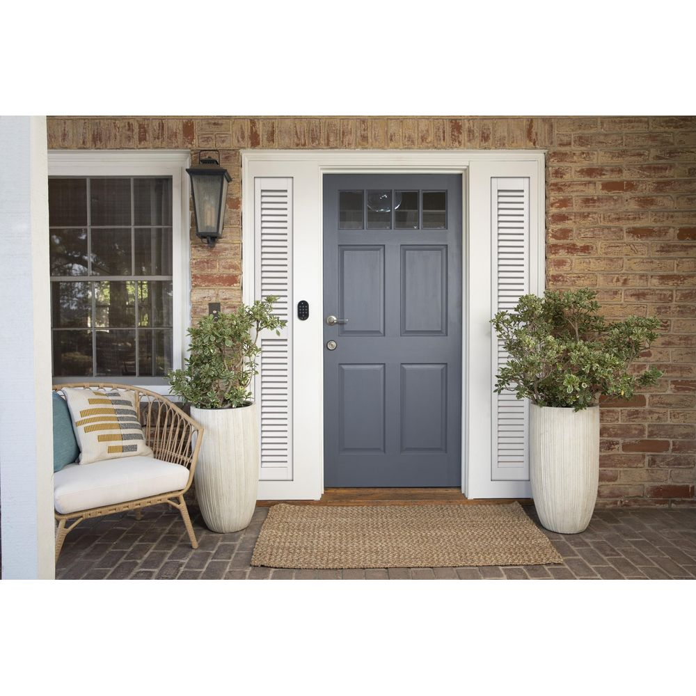 Una puerta principal azul con ventanas, flanqueada por plantas y un sillón.