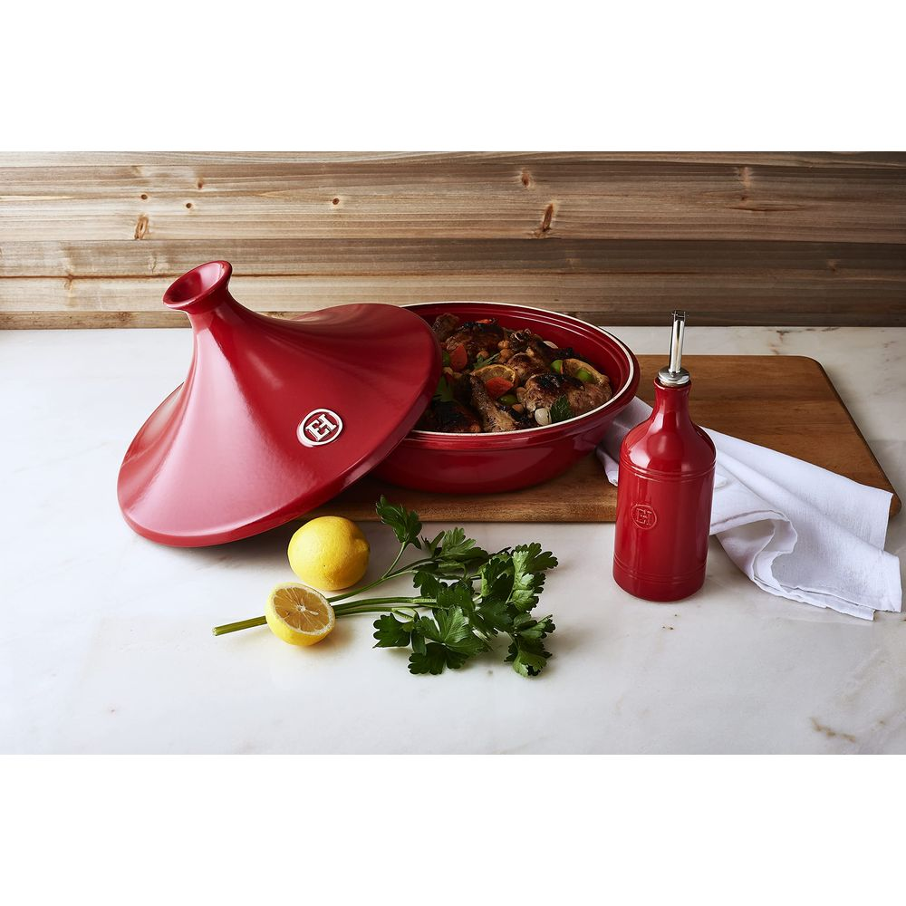 Tajine rosso con cibo, limone, prezzemolo e bottiglia d'olio su tagliere.