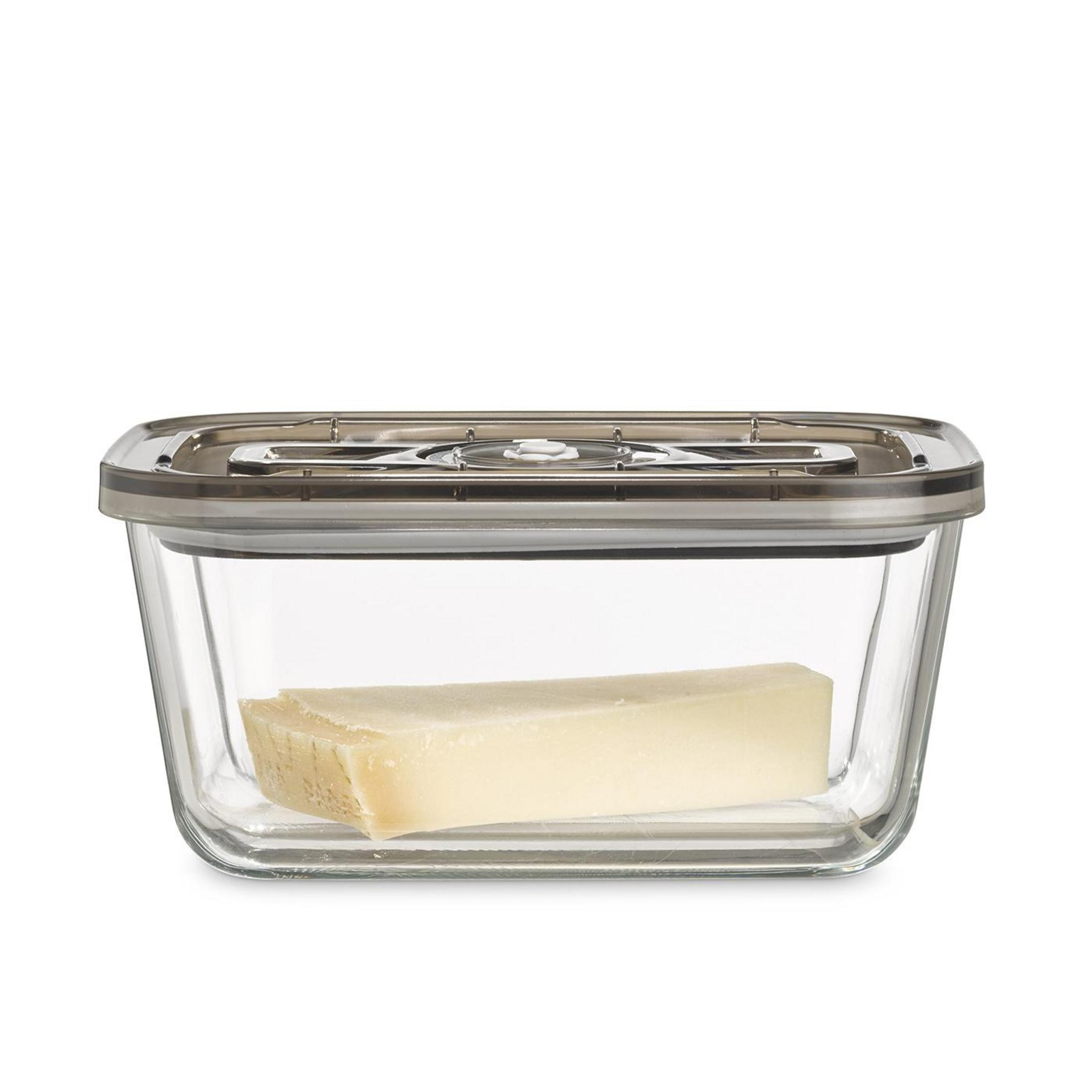 Ein Stück Käse in einem rechteckigen Glasbehälter mit einem dunklen Deckel.
