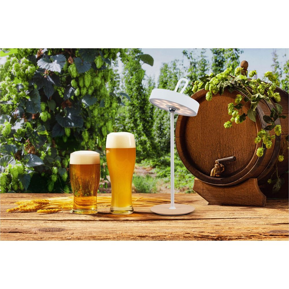 Zwei Gläser Bier, ein Holzbottich, Hopfen und eine Lampe auf einem Holztisch.