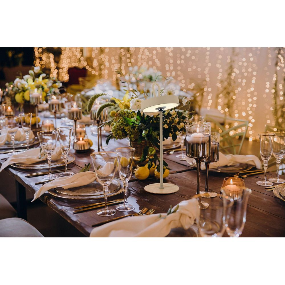 Festlich gedeckter Tisch mit Blumen, Kerzen und Lichterkette im Hintergrund.