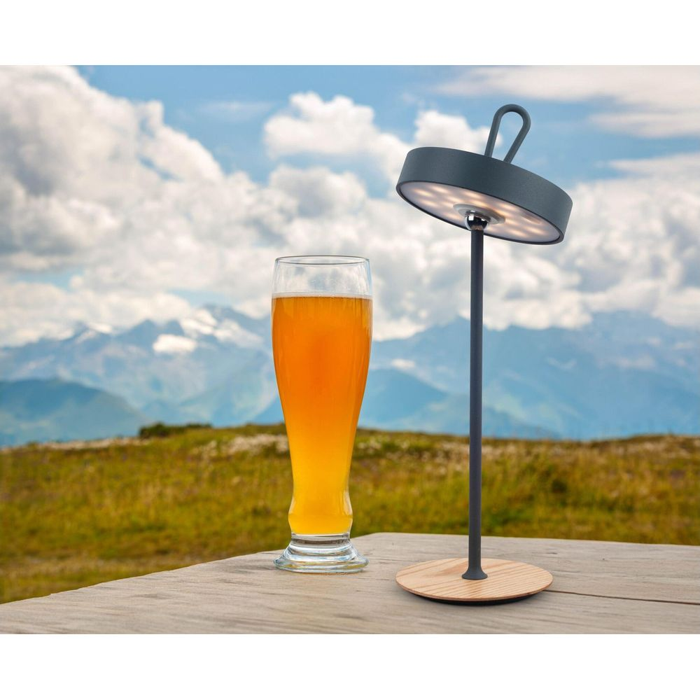 Ein Bierglas und eine Lampe auf einem Holztisch mit Bergen im Hintergrund.