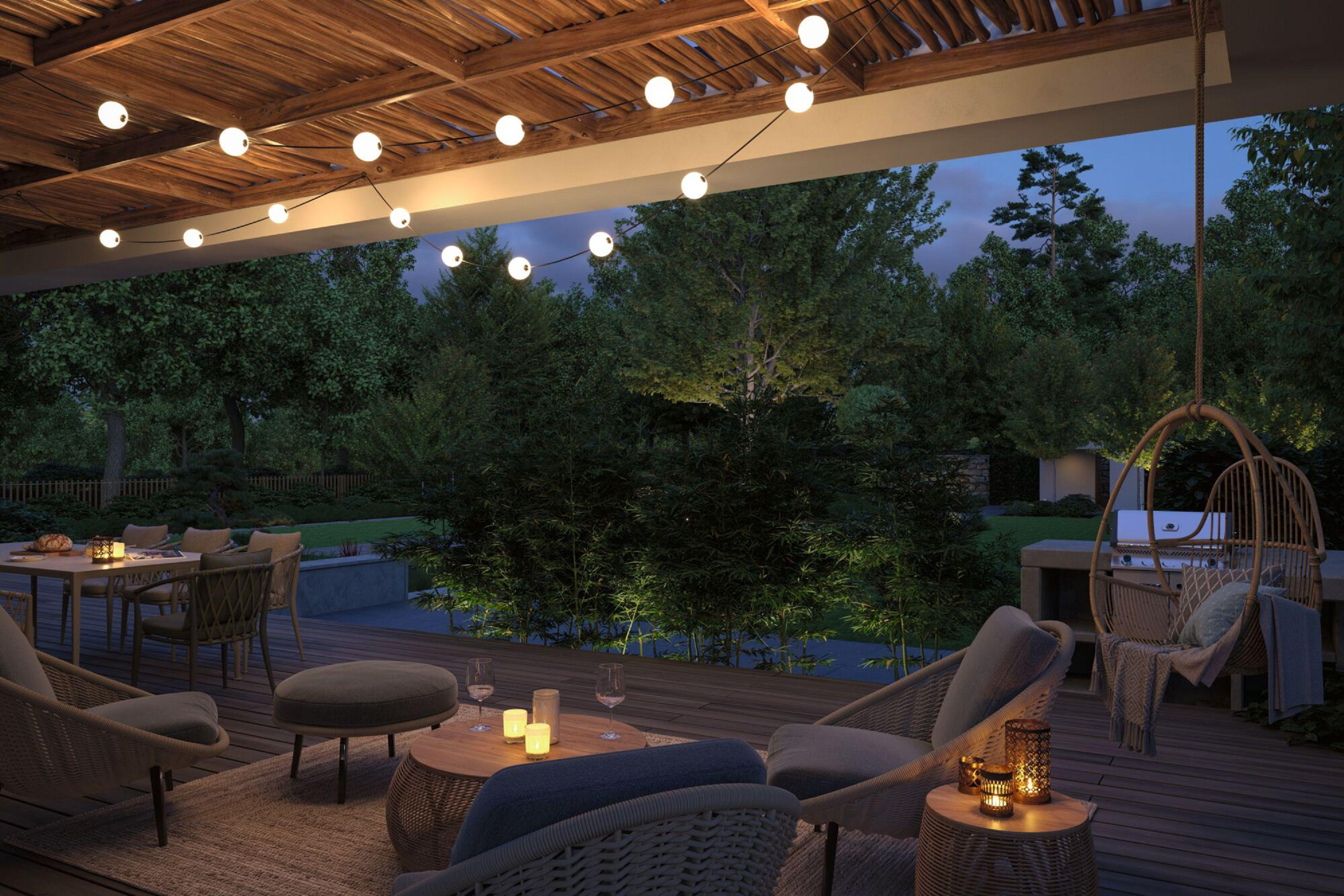 Patio nocą z fotelem wiszącym, siedzeniami, światłami i drzewami.