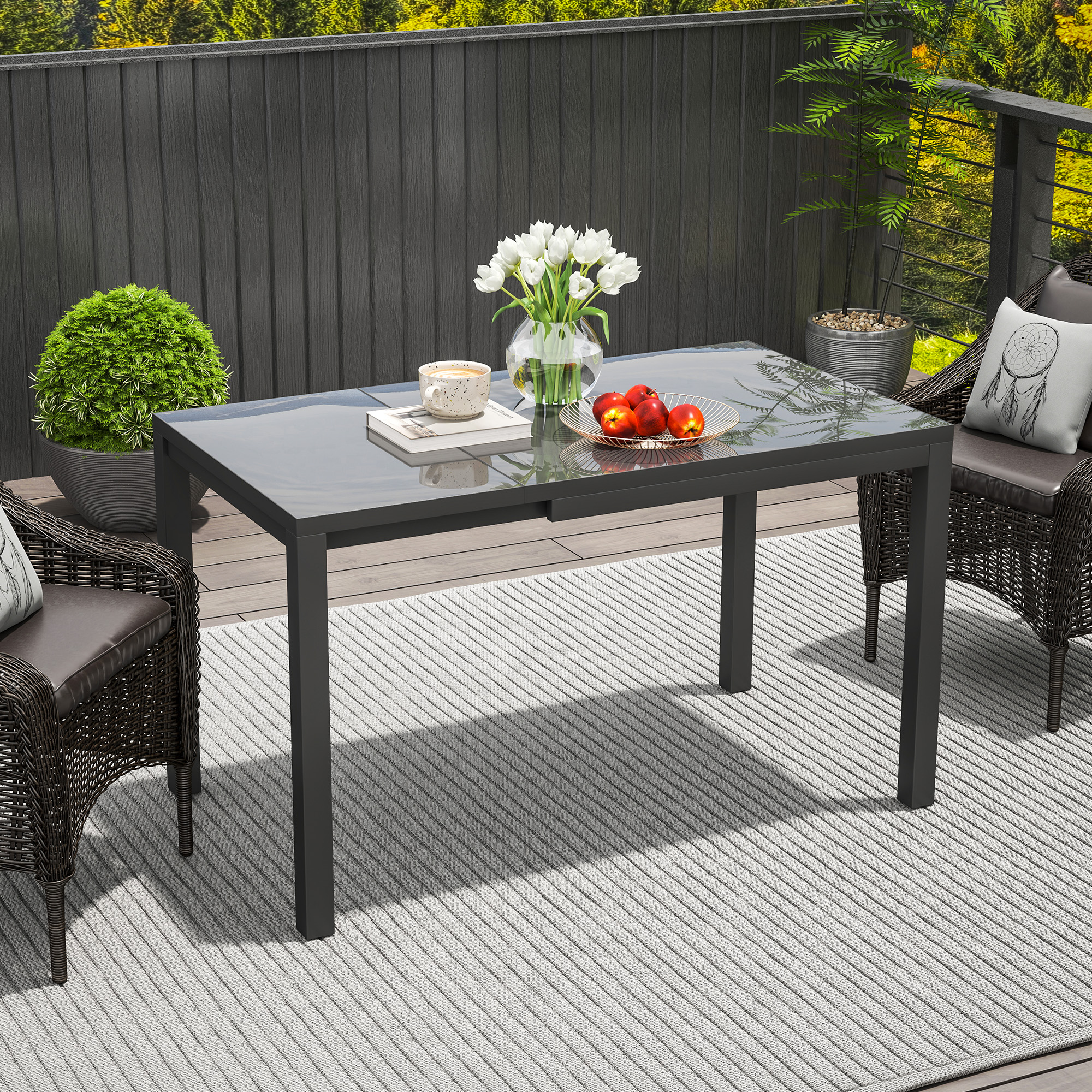 Mesa de comedor de vidrio y metal para exteriores con flores, fruta y taza.