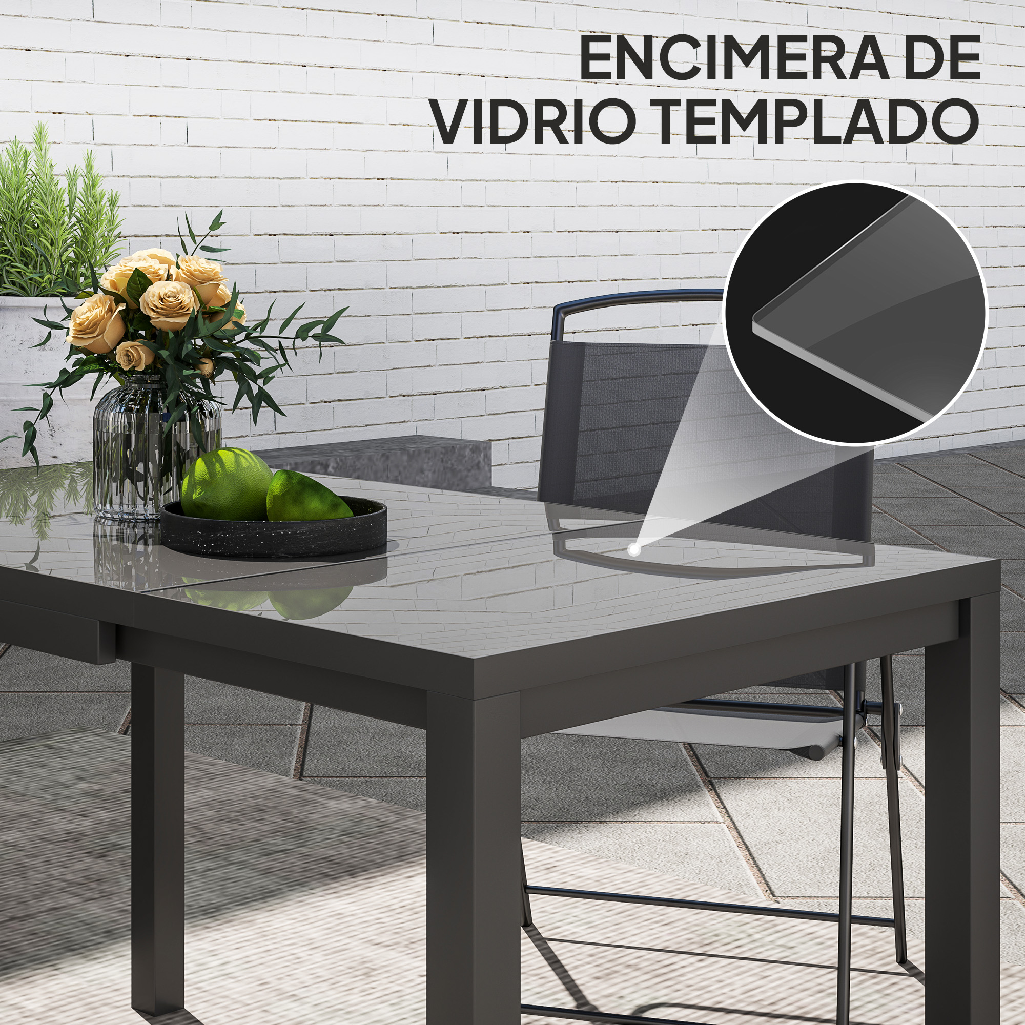Mesa gris con tapa de cristal, flores y fruta frente a pared de ladrillos.