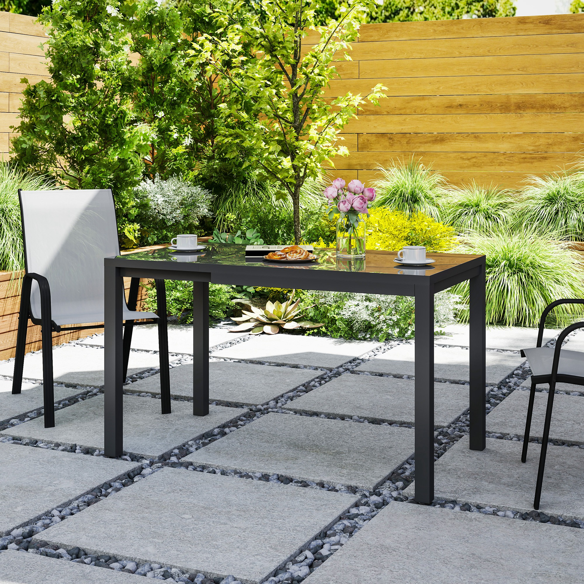 Mesa de patio con sillas, sobre un patio de piedra con vegetación y valla de madera.