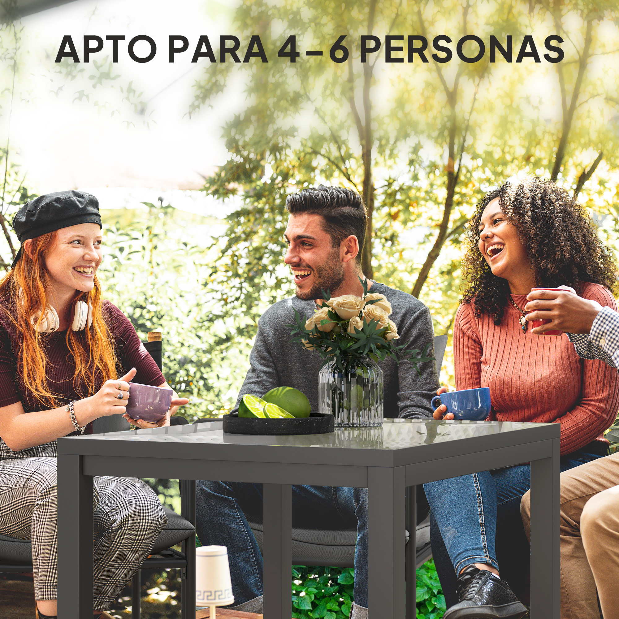 Cuatro amigos riendo se sientan al aire libre en una mesa con bebidas y fruta.