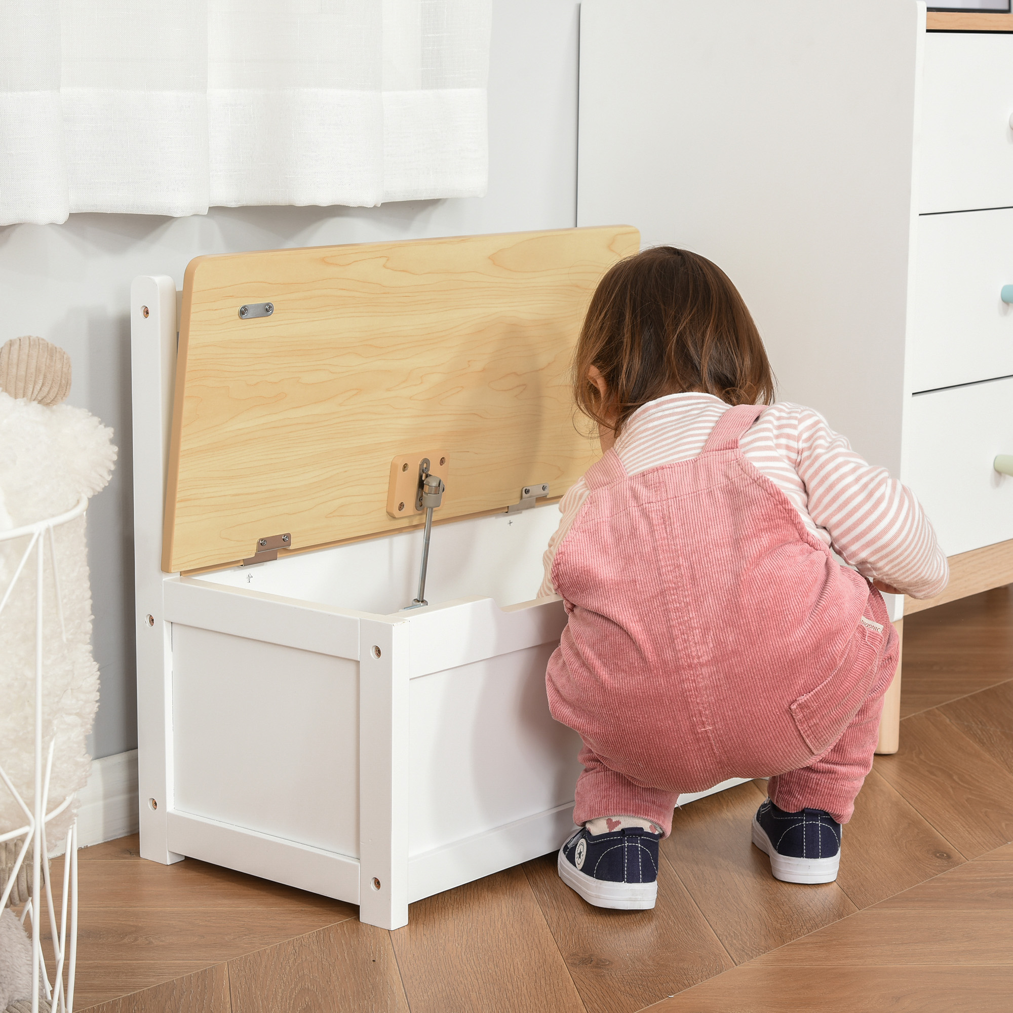 Un niño con peto mira dentro de un baúl blanco abierto con tapa de madera.