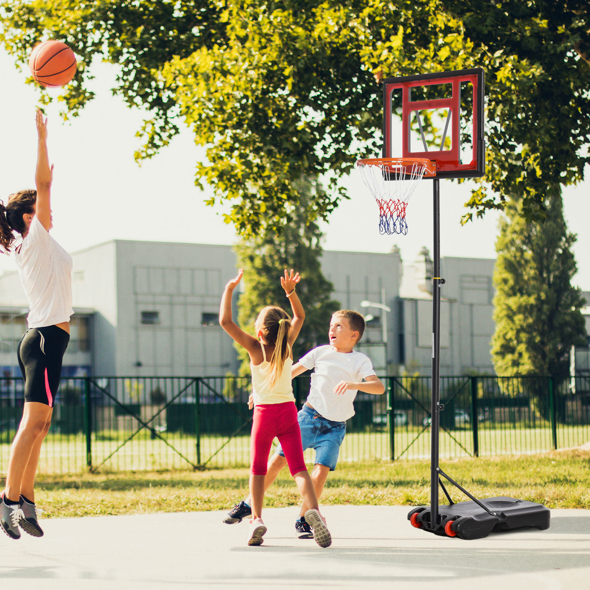 Mujer lanza balón, niños juegan baloncesto en cancha exterior.