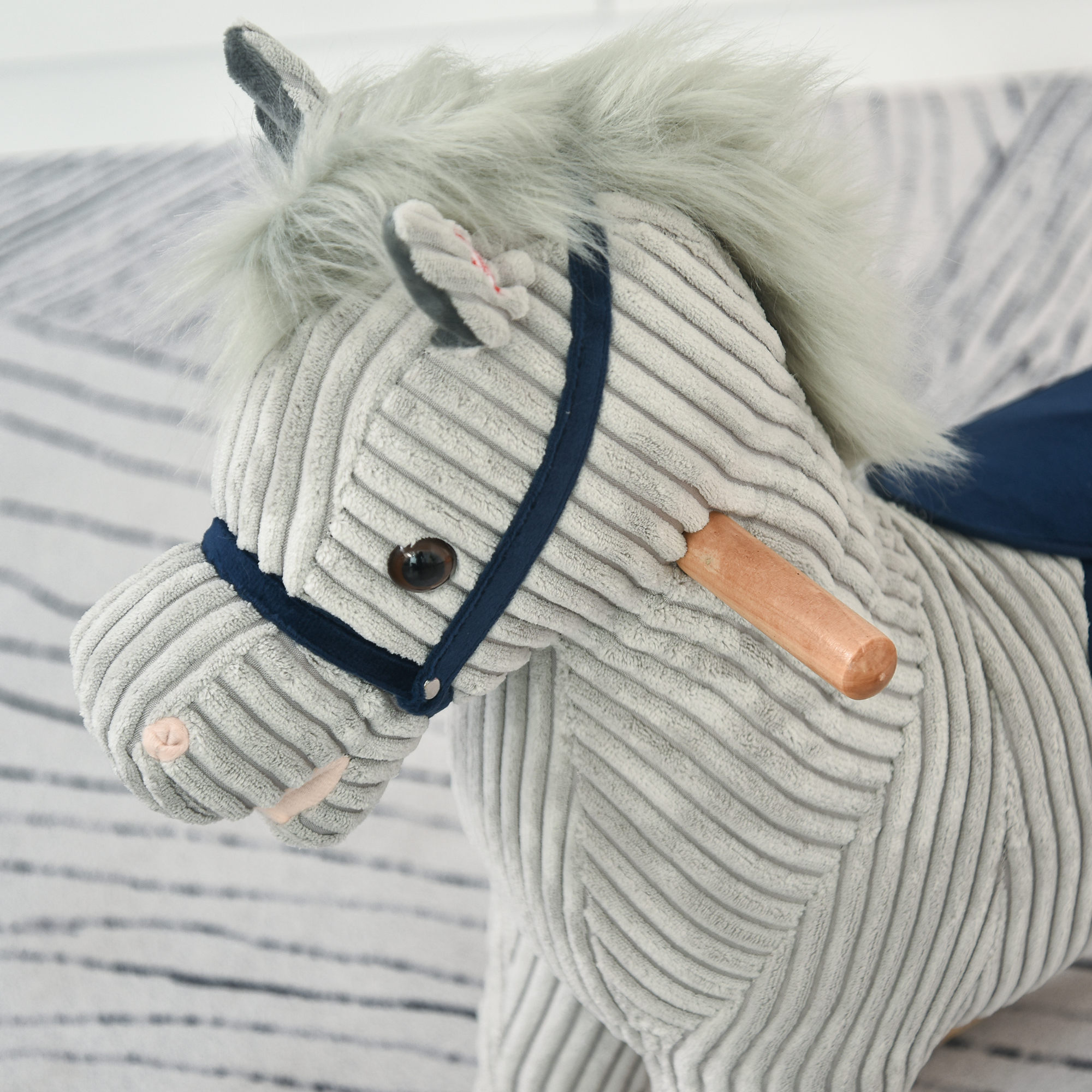 Caballo balancín gris de pana con crin de peluche, brida azul y asas.