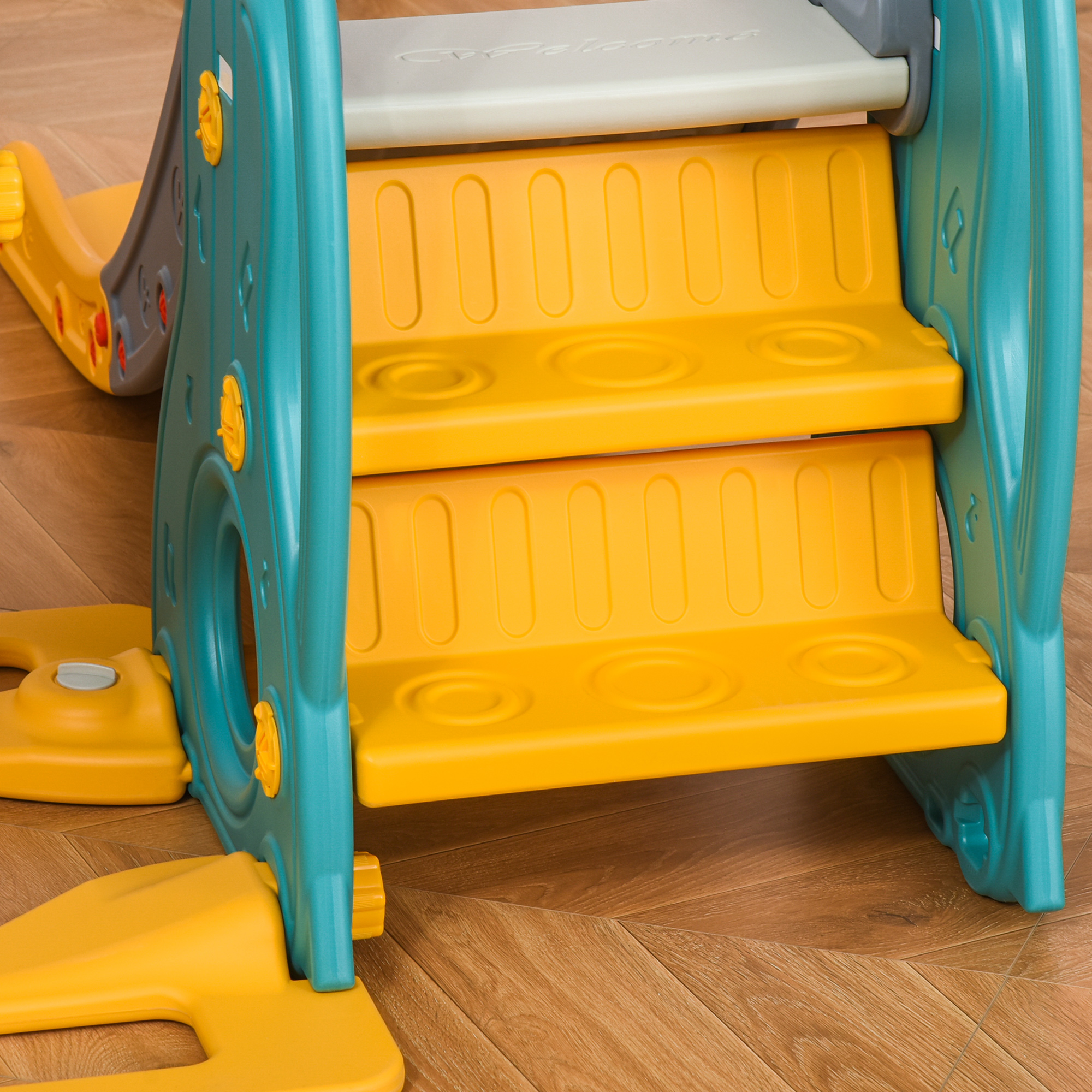 Estructura de tobogán infantil turquesa y amarilla con escalones en suelo de madera.