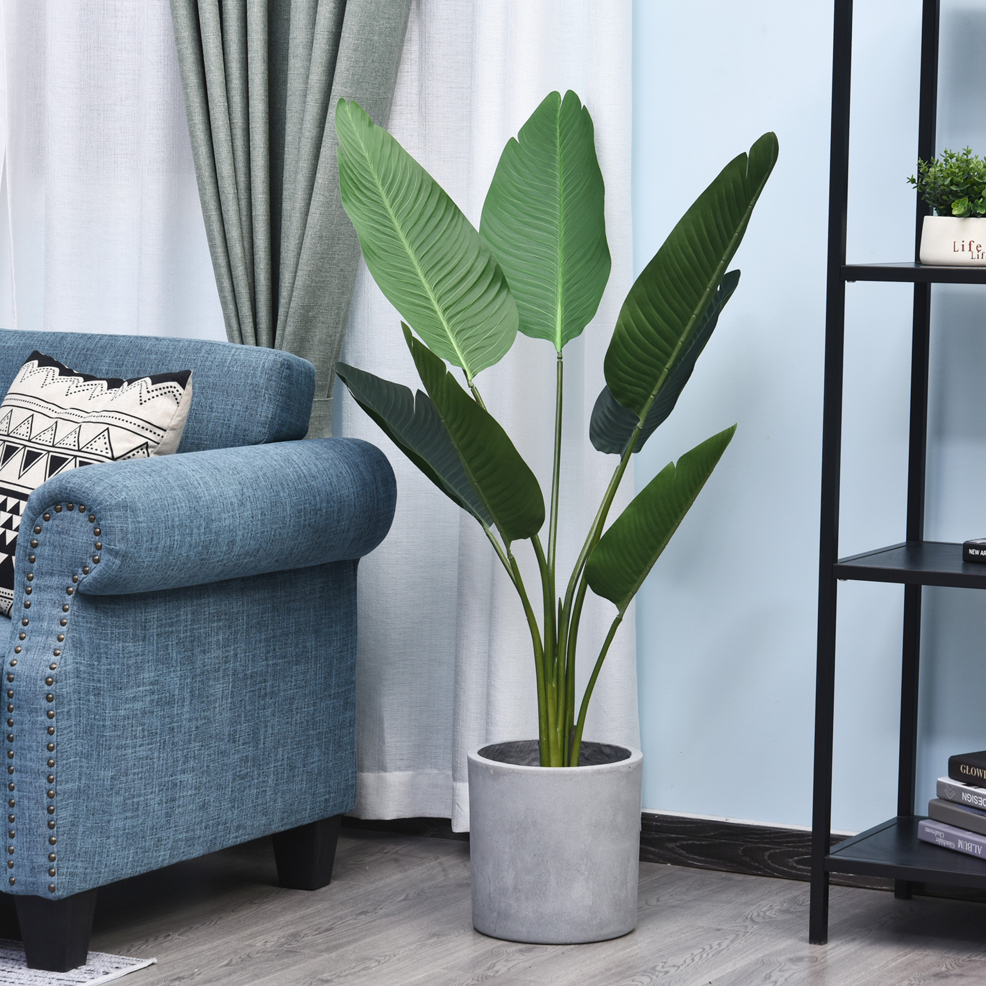 Un sillón azul con cojín junto a una planta grande en maceta y un estante negro.