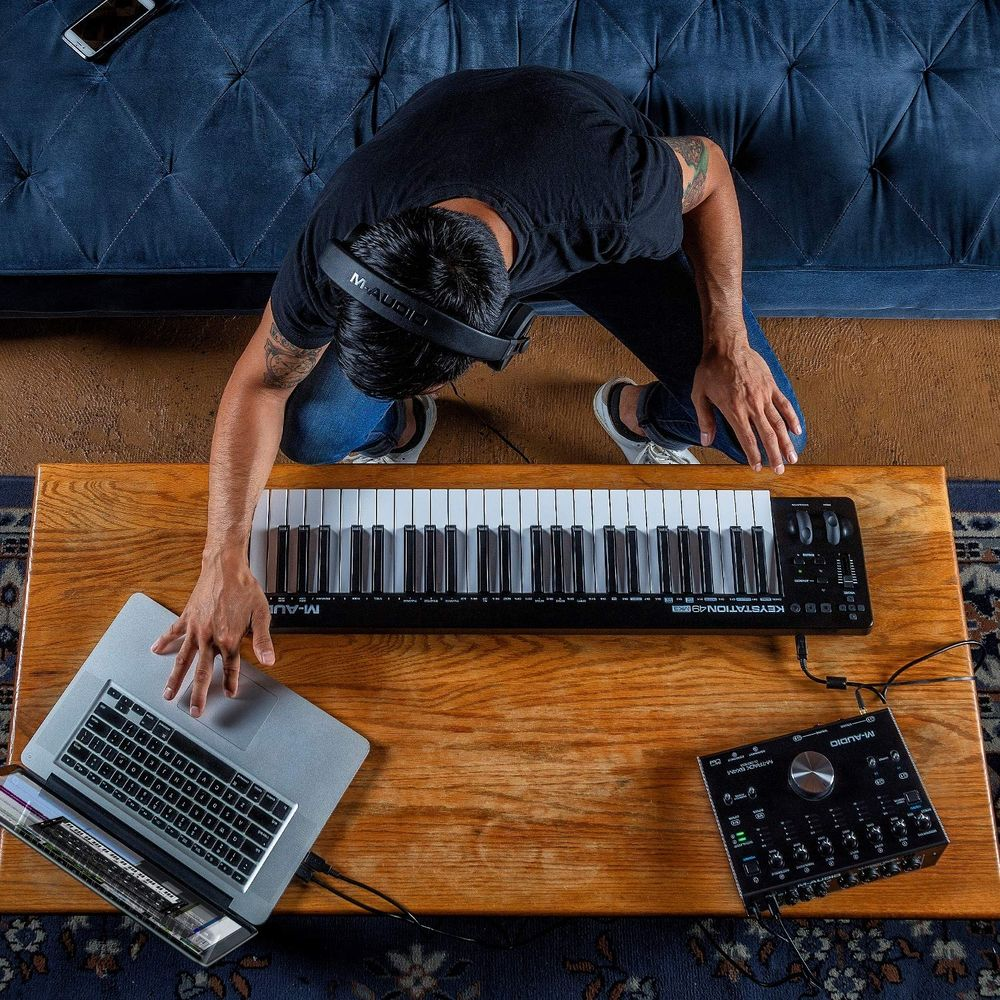 Mężczyzna w słuchawkach klęczy przy klawiaturze i laptopie. Obok czarny interfejs audio.