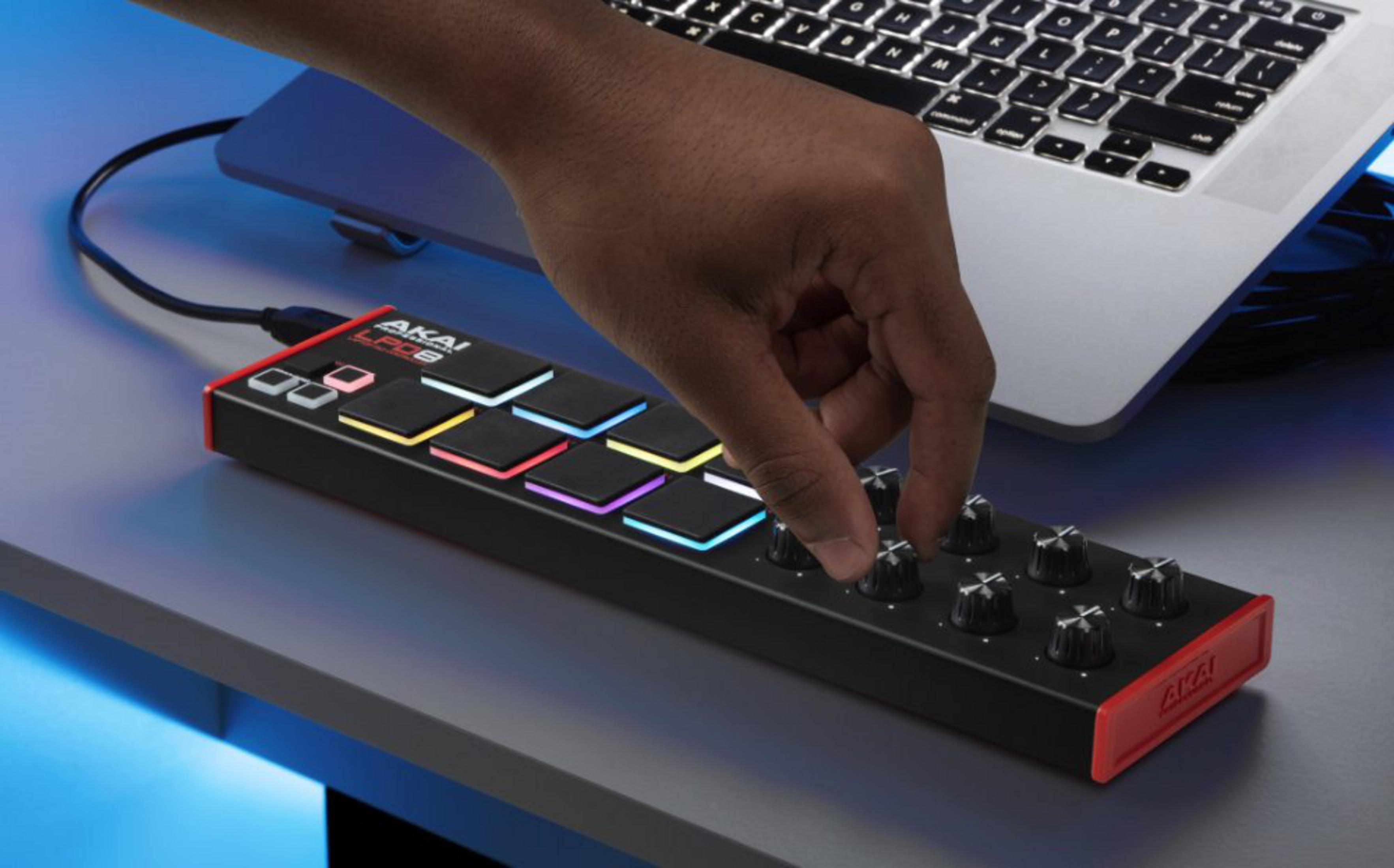Dłoń reguluje pokrętła na czarnym kontrolerze MIDI z kolorowymi podświetlanymi padami, podłączonym do laptopa.