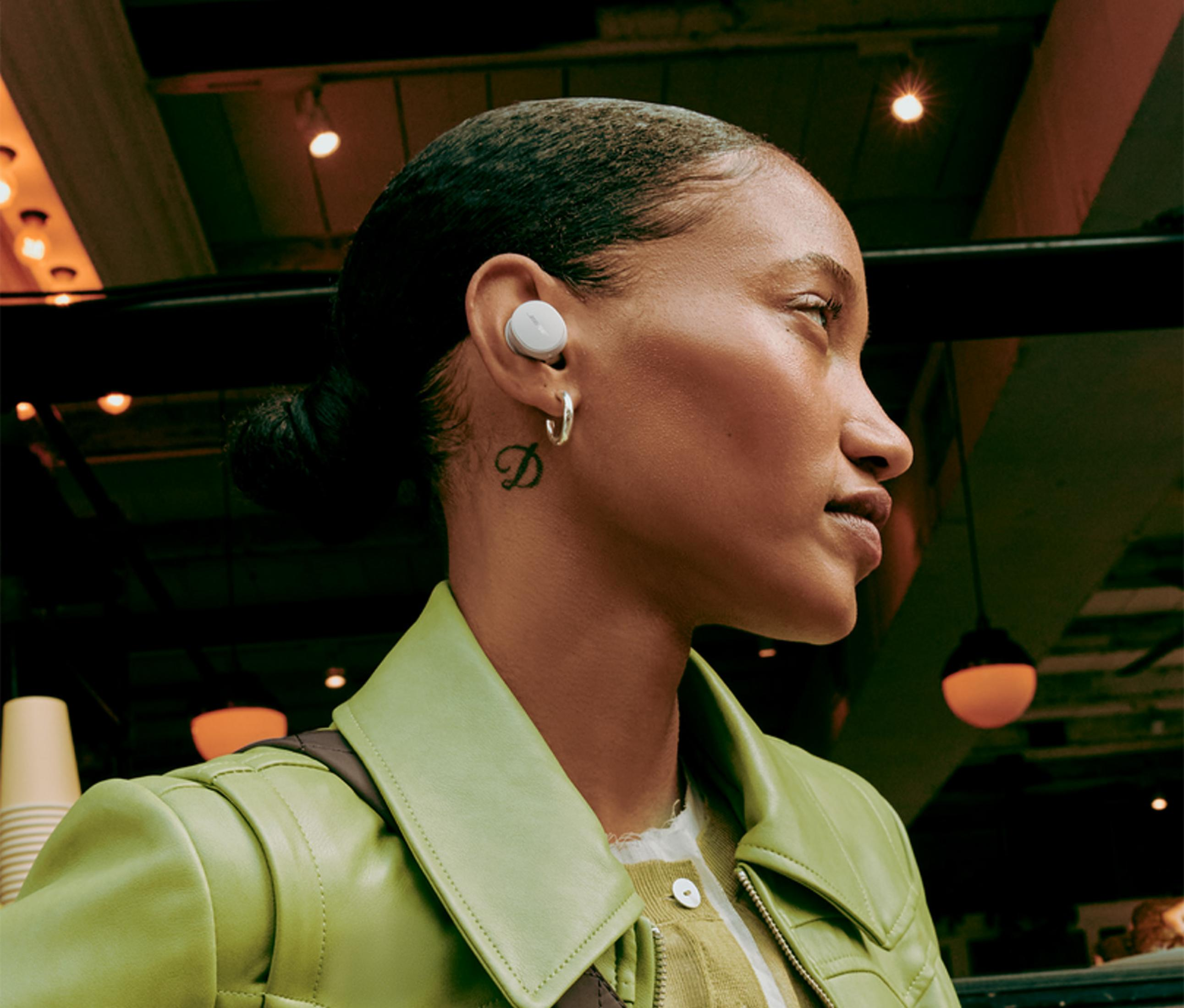 Mujer con auricular, chaqueta verde, fondo con luces.