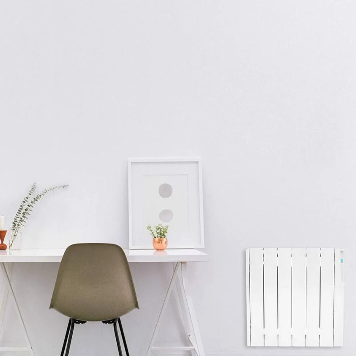 Un escritorio blanco con silla, arte enmarcado y un radiador blanco en una pared blanca.