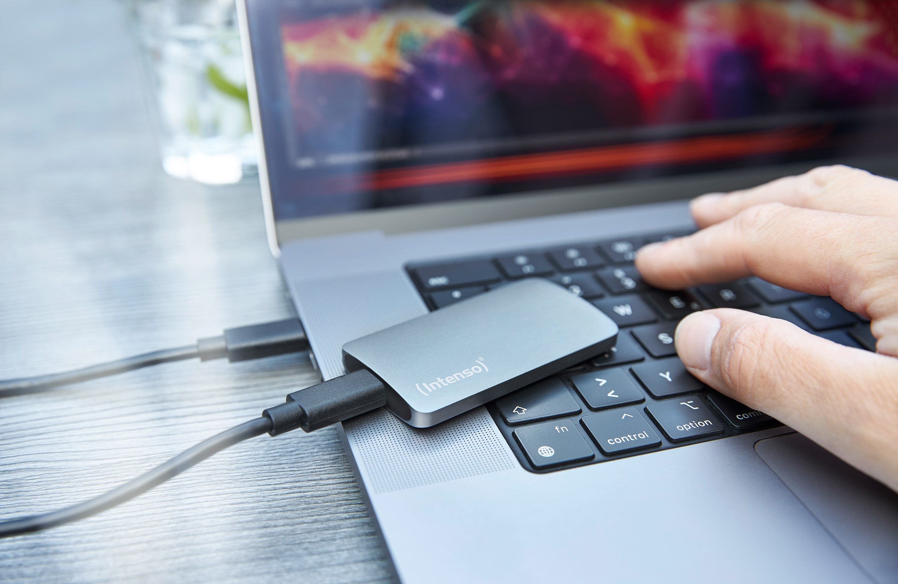 Laptop z dyskiem zewnętrznym podłączonym przez USB. Ręka pisze na klawiaturze.