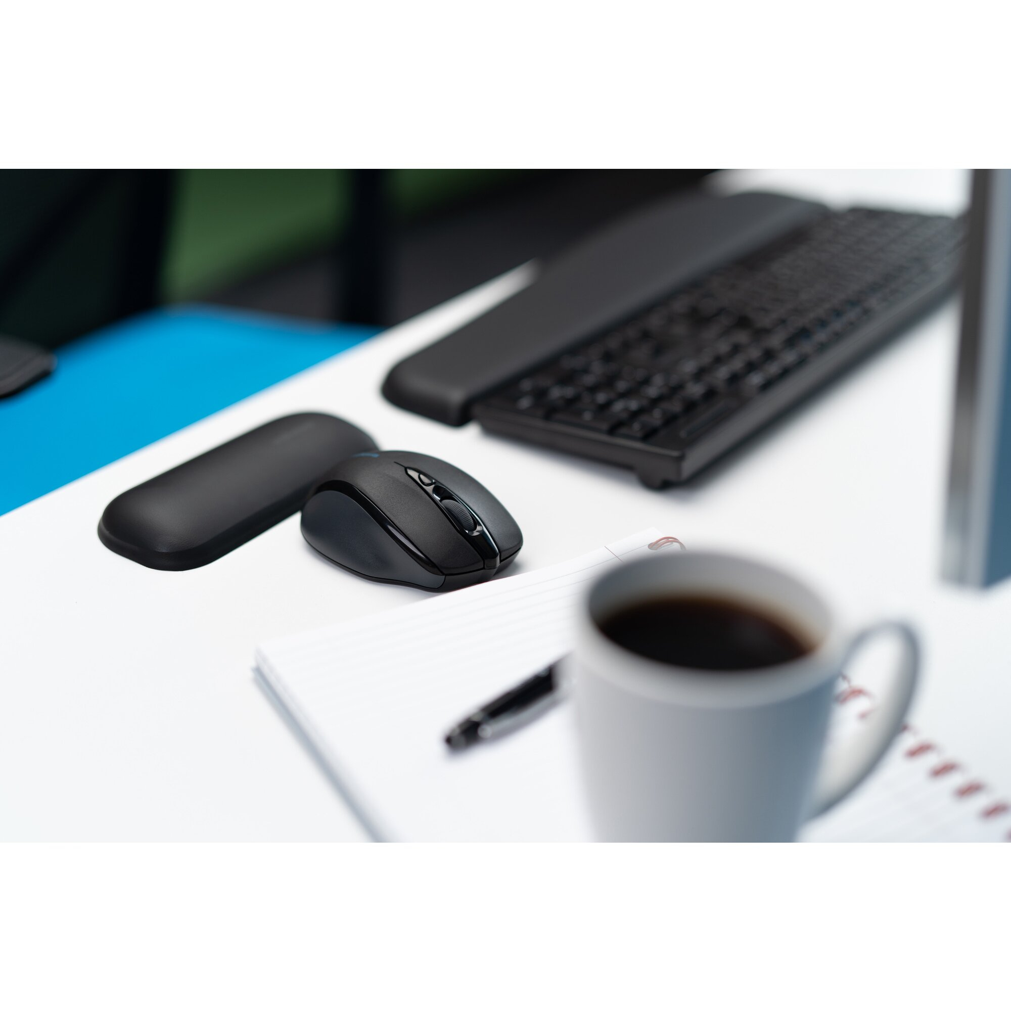 Ratón y teclado negros sobre escritorio blanco con taza de café.