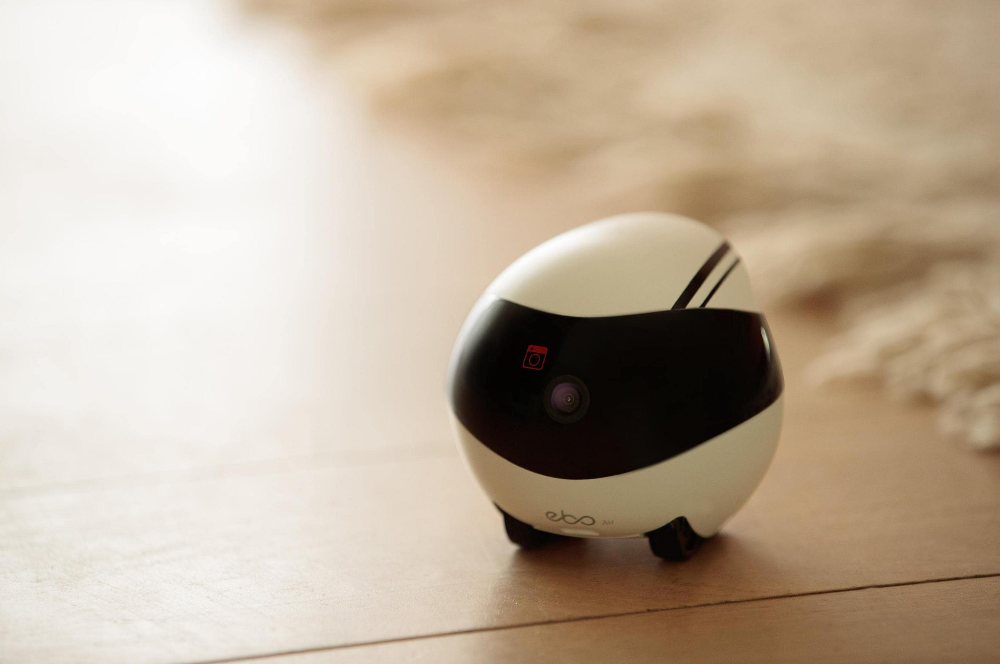 Biały robot z czarną maską i kamerą na drewnianej podłodze.