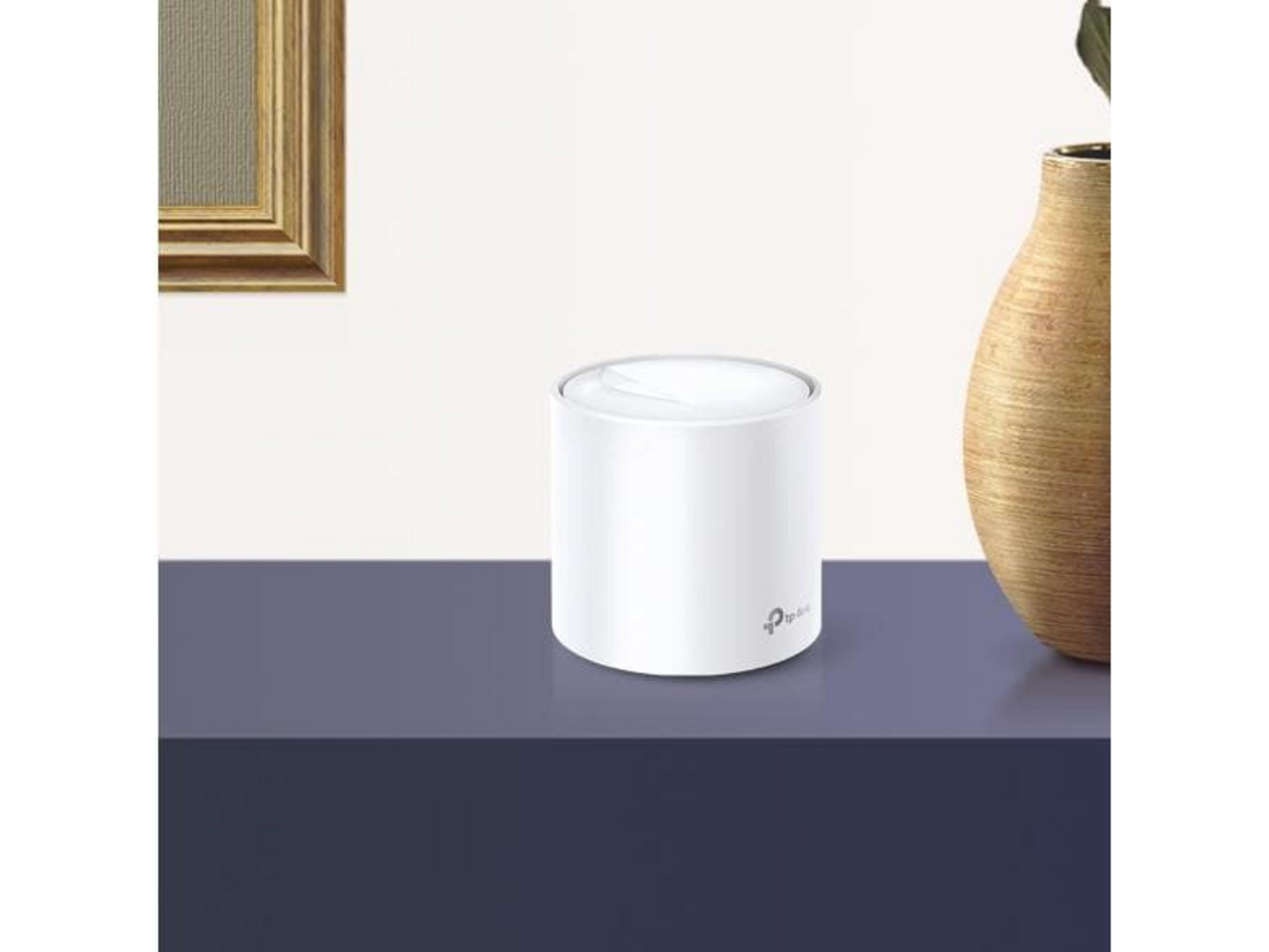 Ein weißer zylindrischer Router steht auf einem blauen Tisch neben einer Vase.