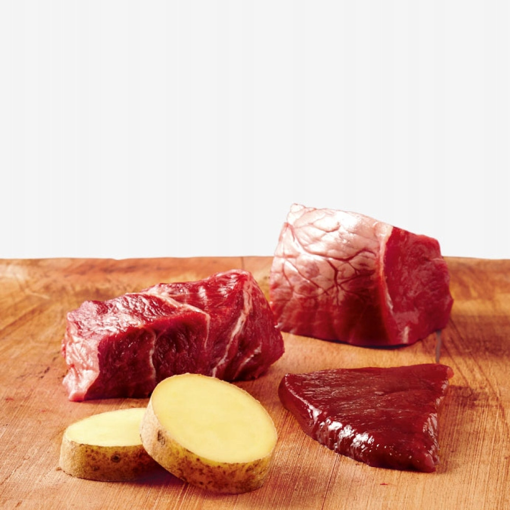 Surowe kawałki wołowiny i plasterki ziemniaków na drewnianej desce.