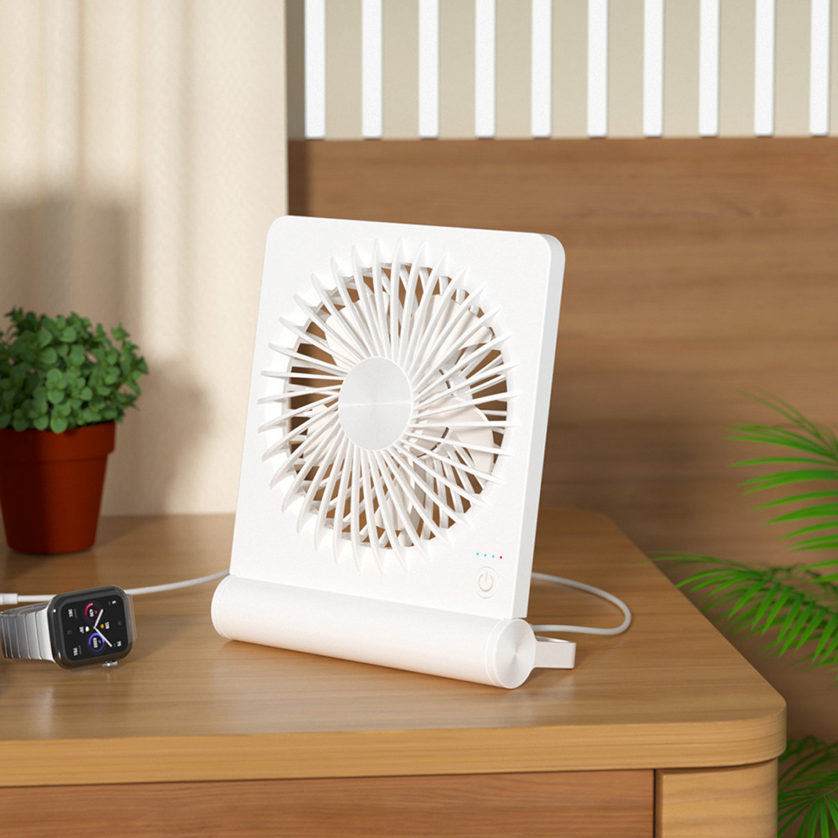 Ein weißer Tischventilator mit einem Smartwatch daneben auf einem Holztisch.