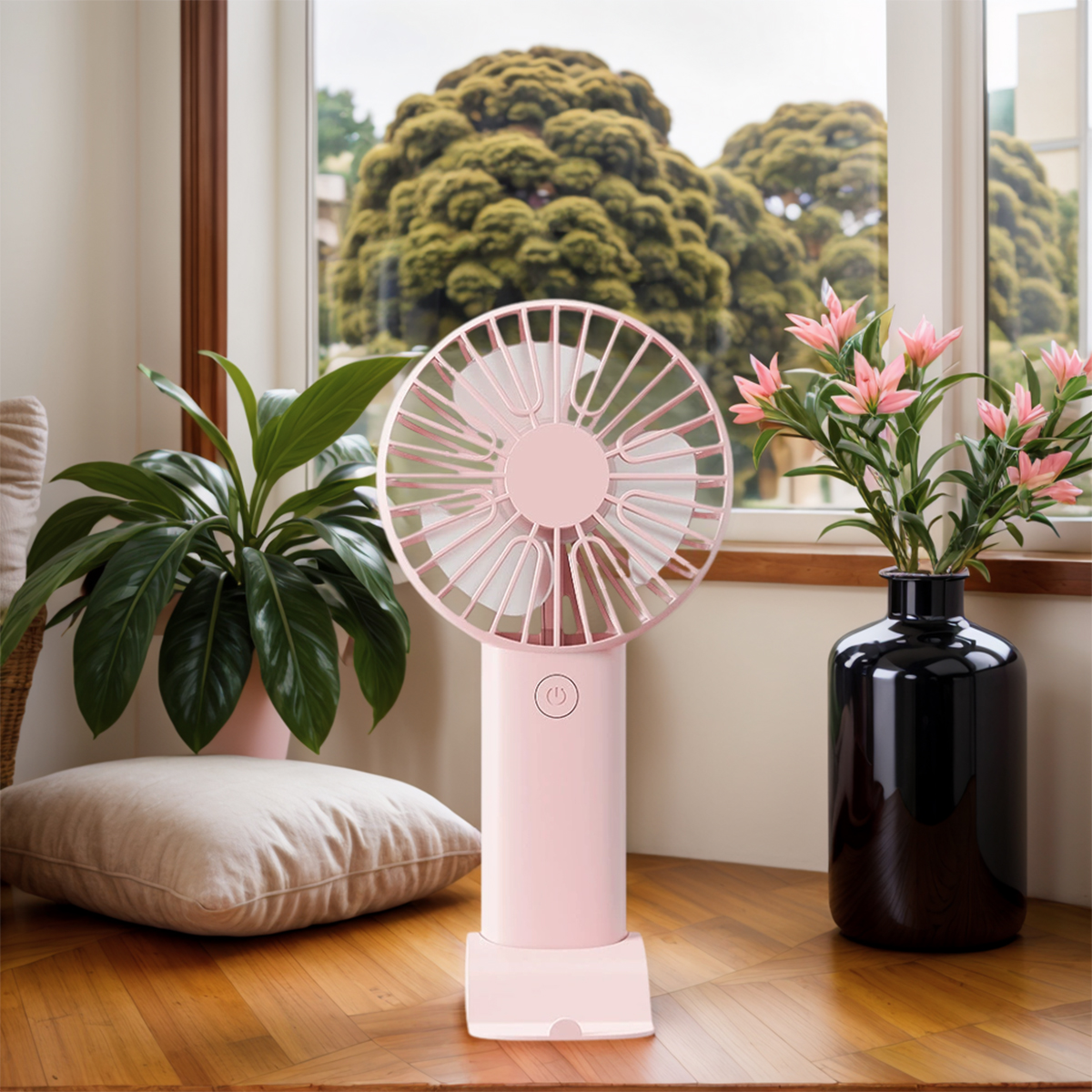 Ein rosafarbener Ventilator steht neben einer grünen Pflanze und einer schwarzen Vase mit Blumen.