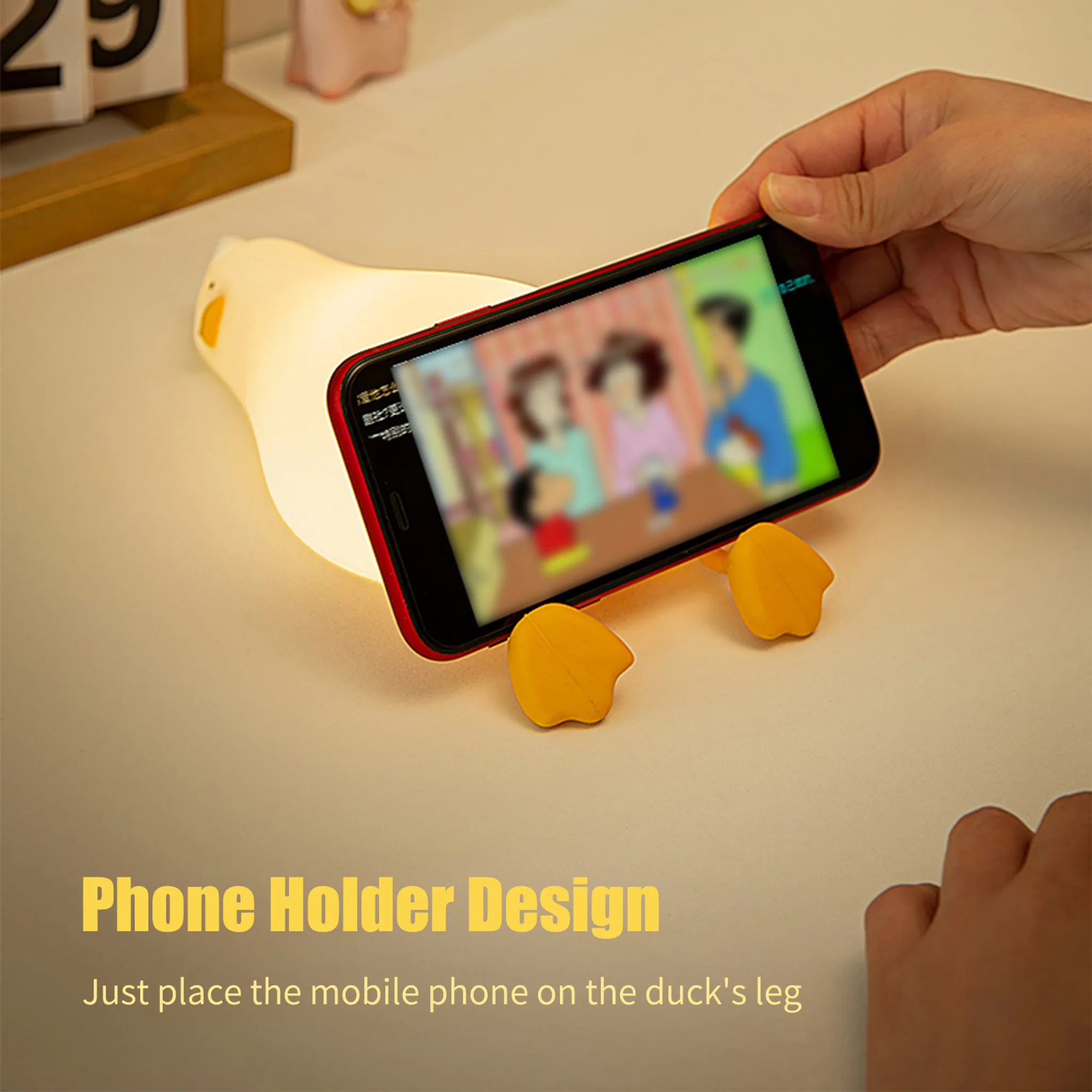 Ein Handy ruht auf den Füßen einer leuchtenden gelben Entenlampe.