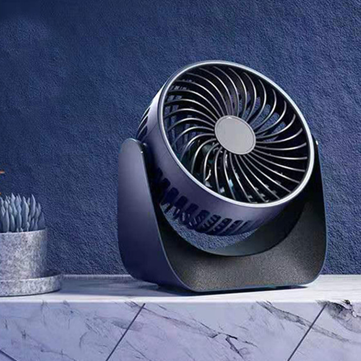 Ein kleiner, dunkler Ventilator steht auf einem Marmortisch vor einer blauen Wand.