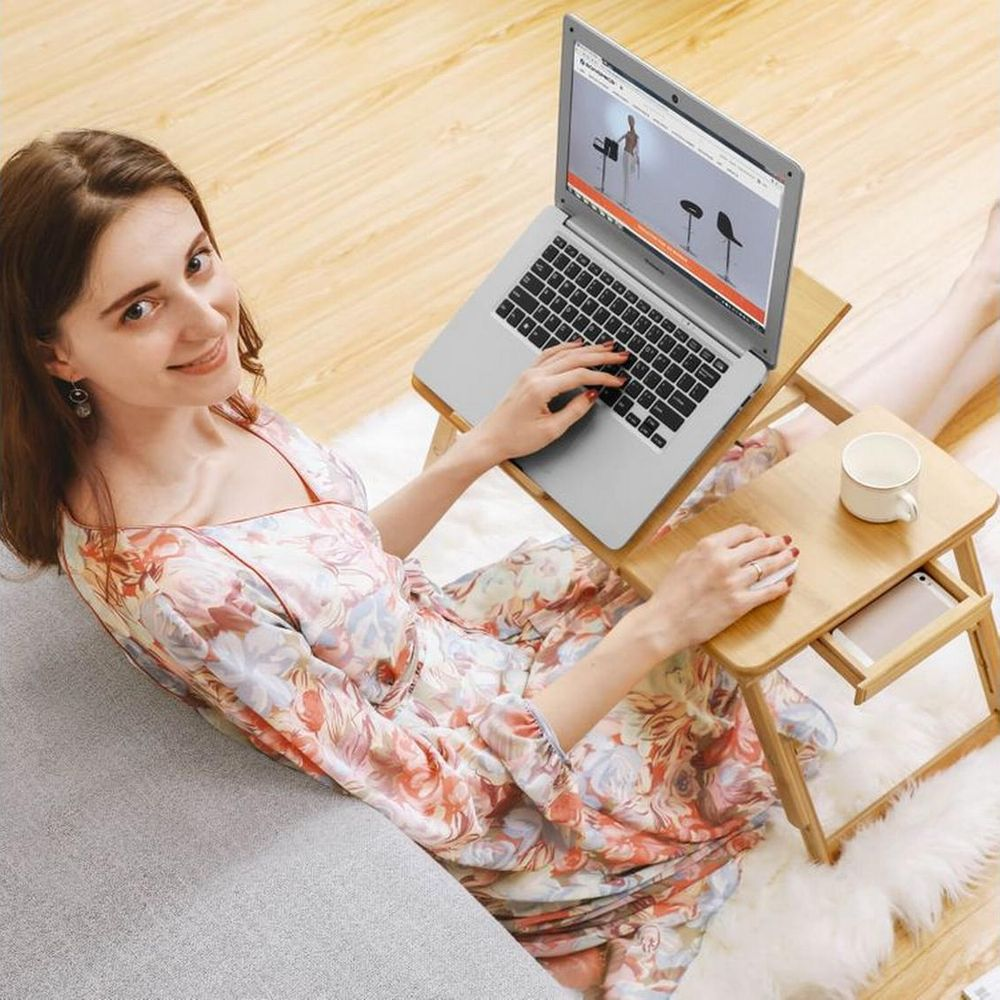 Eine Frau sitzt auf einem Teppich und benutzt einen Laptop auf einem Holztisch.
