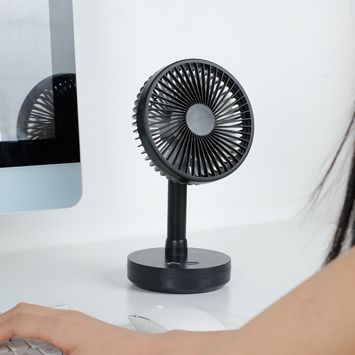 Ein schwarzer Schreibtischventilator steht neben einem Computermonitor auf einem weißen Schreibtisch.