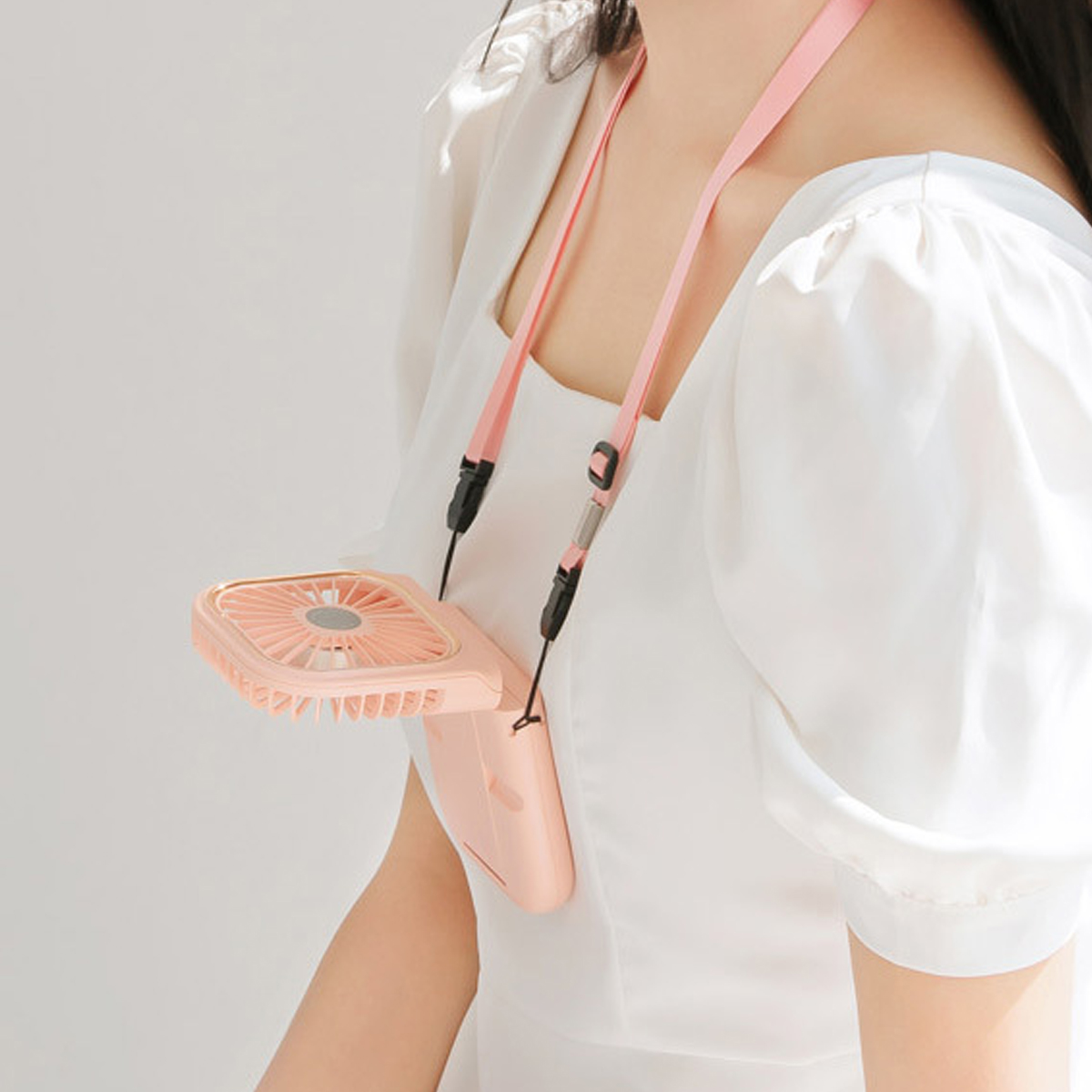 Eine Person trägt einen rosa Nackenventilator an einem Band über einem weißen Kleid.