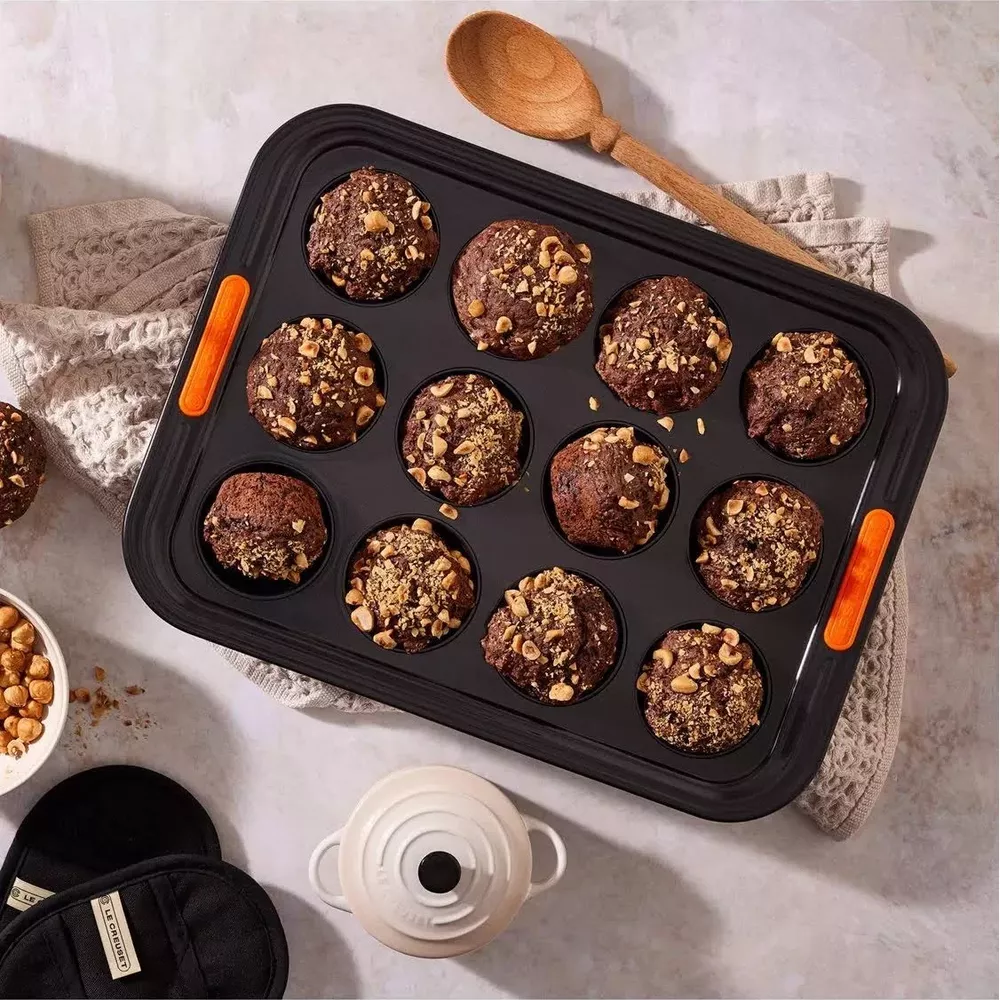 Schokoladenmuffins mit Nüssen in einem Muffinblech, mit Holzlöffel.