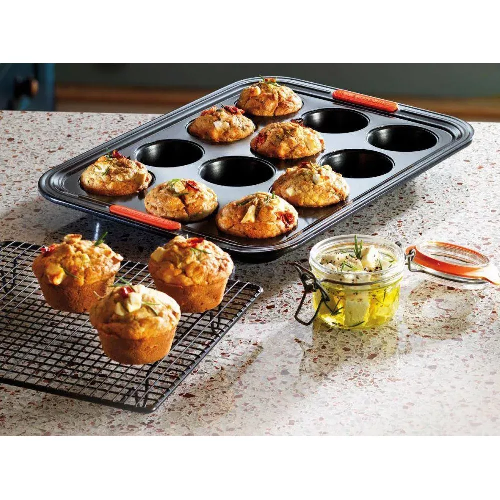 Muffins in einer Backform und auf einem Rost, neben einem Glas mit mariniertem Käse.