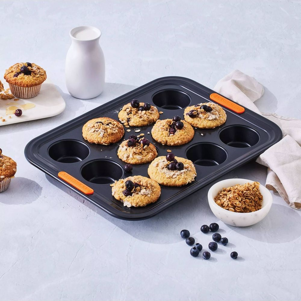 Ein Muffinform mit Blaubeermuffins, Haferflocken und einer Karaffe Milch.