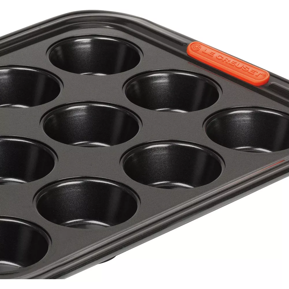 Eine schwarze Muffinform mit 12 Mulden und einem orangen Griff mit Le Creuset Logo.