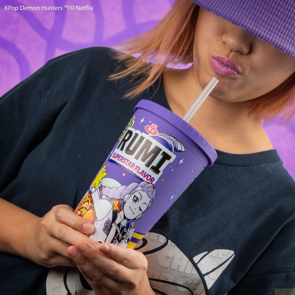 Una persona con pelo rosa sostiene un vaso morado con la etiqueta RUMI.