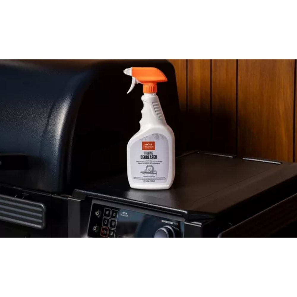 Eine weiße Sprühflasche mit orangem Griff steht auf einem schwarzen Grill.