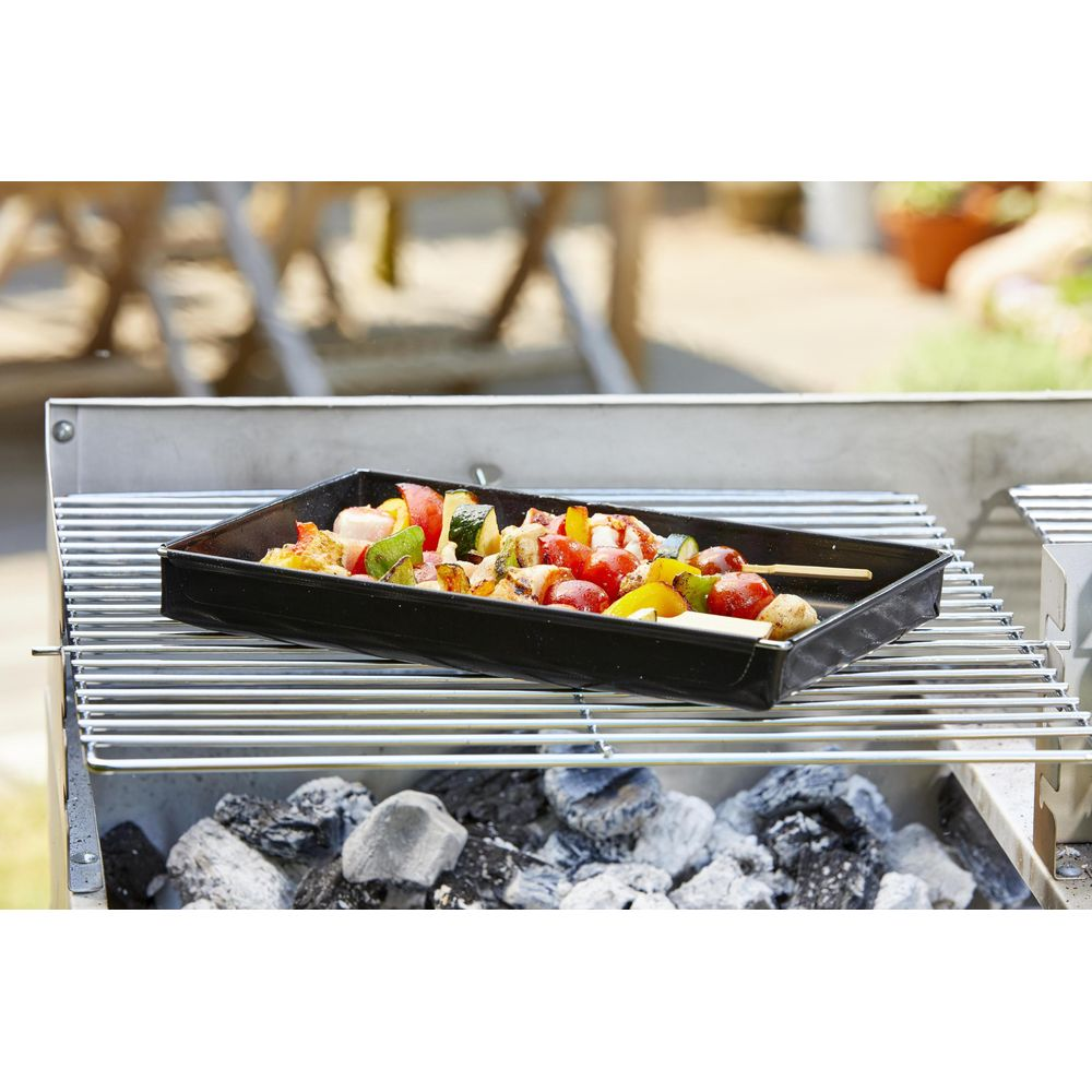 Ein Grill mit einer schwarzen Schale voller Spieße mit Gemüse und Garnelen.